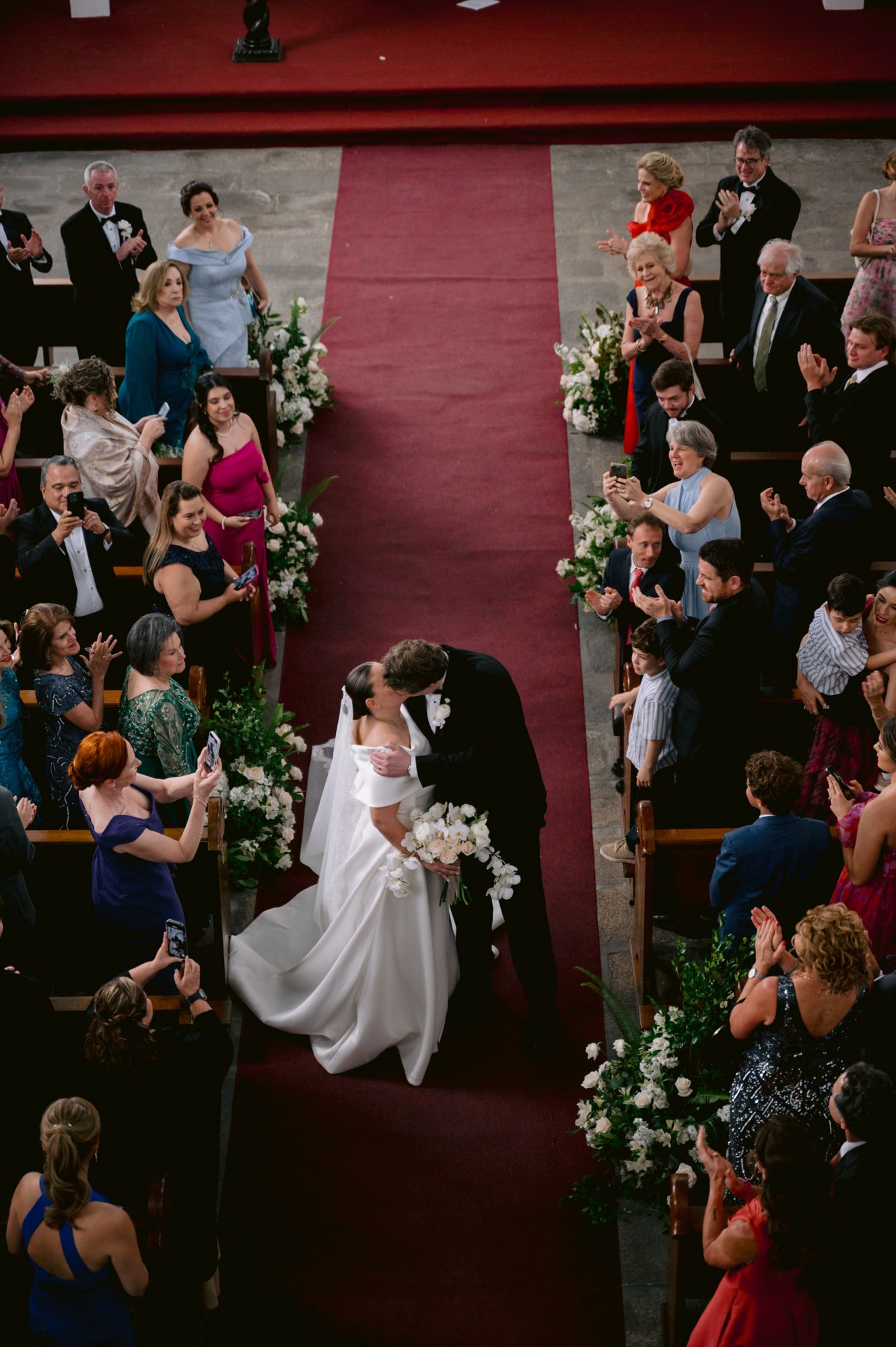 Bird's eye view of a wedding ceremony in a church with guests lining the red-carpeted aisle.