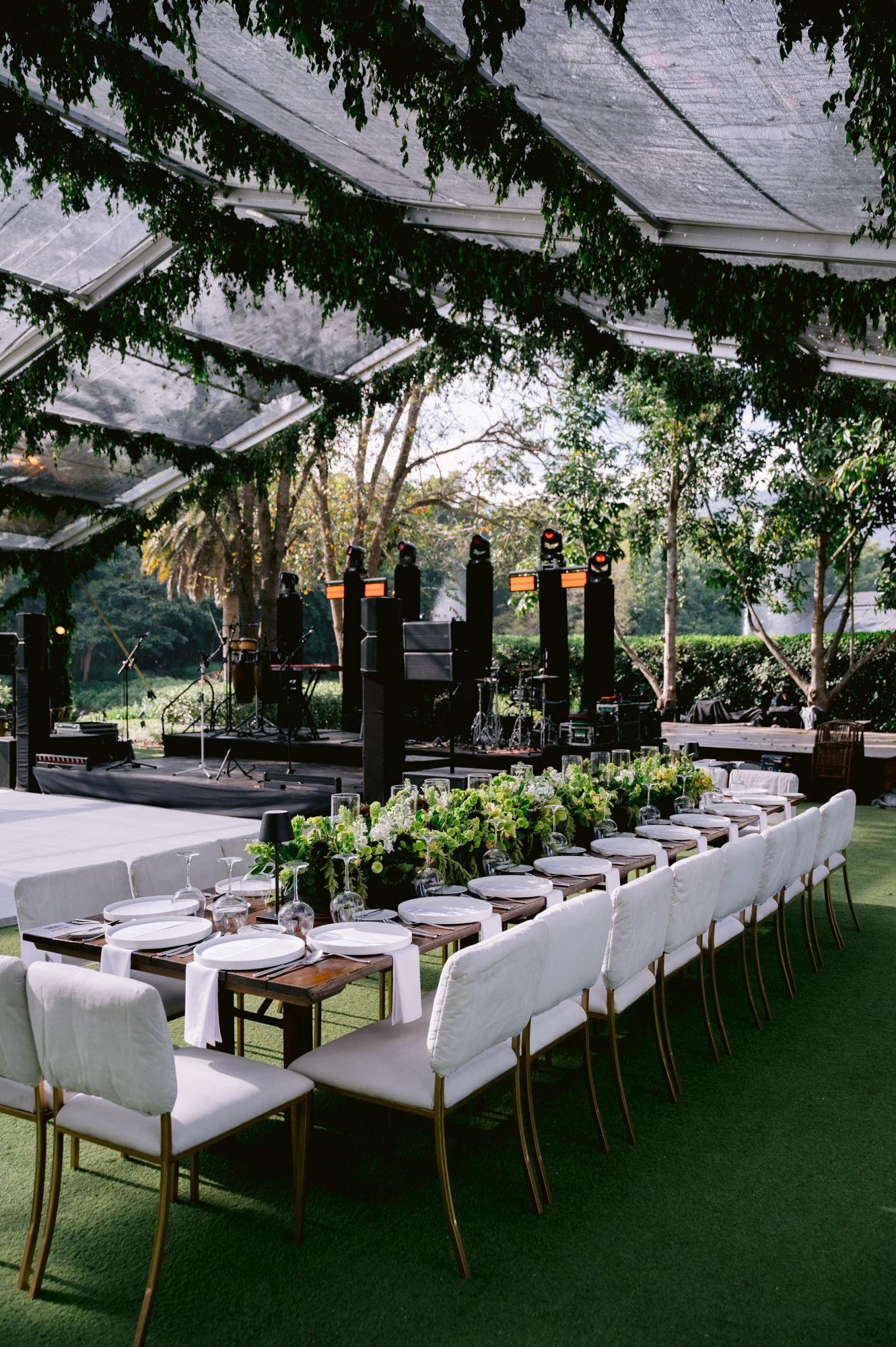 Elegant outdoor wedding reception setup with white chairs and clear tent covering over artificial grass flooring.