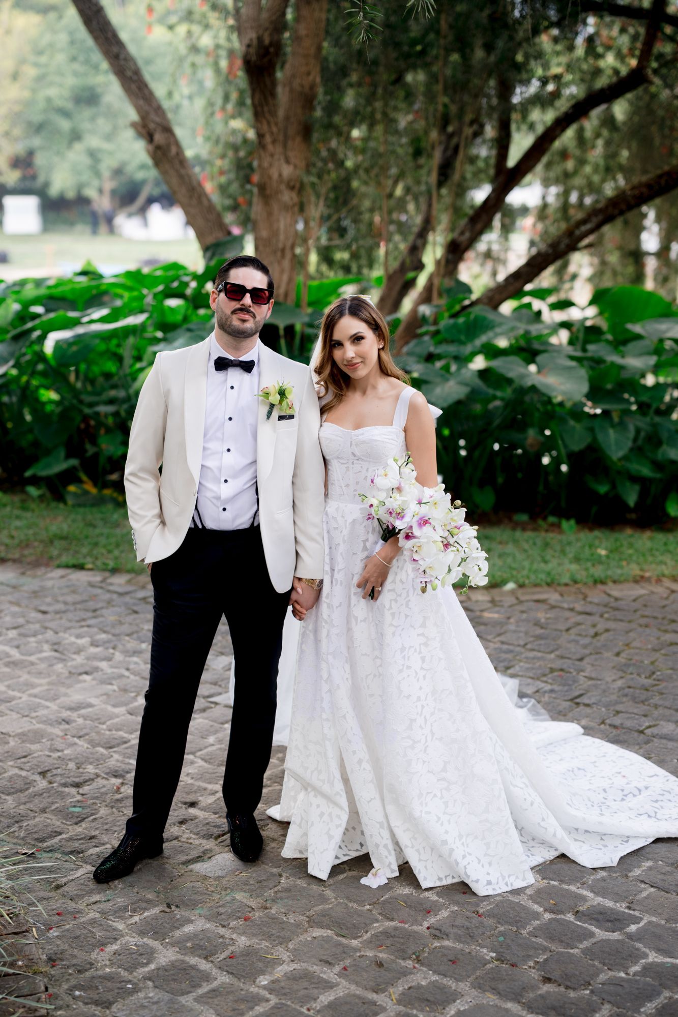 A couple poses for wedding photos on a stone path surrounded by lush greenery.