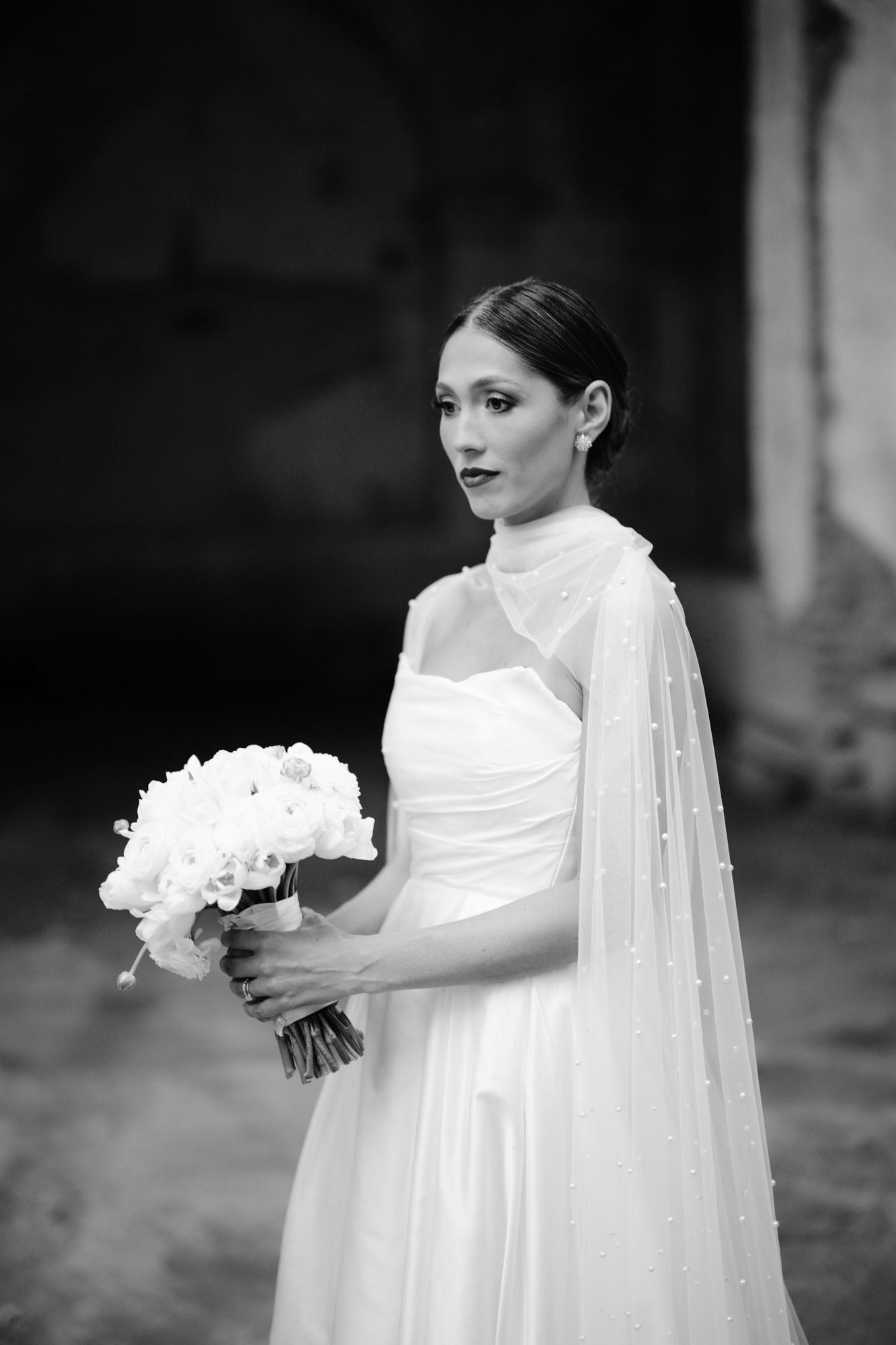 Black and white portrait of bride holding white bouquet wearing sleek modern wedding gown.