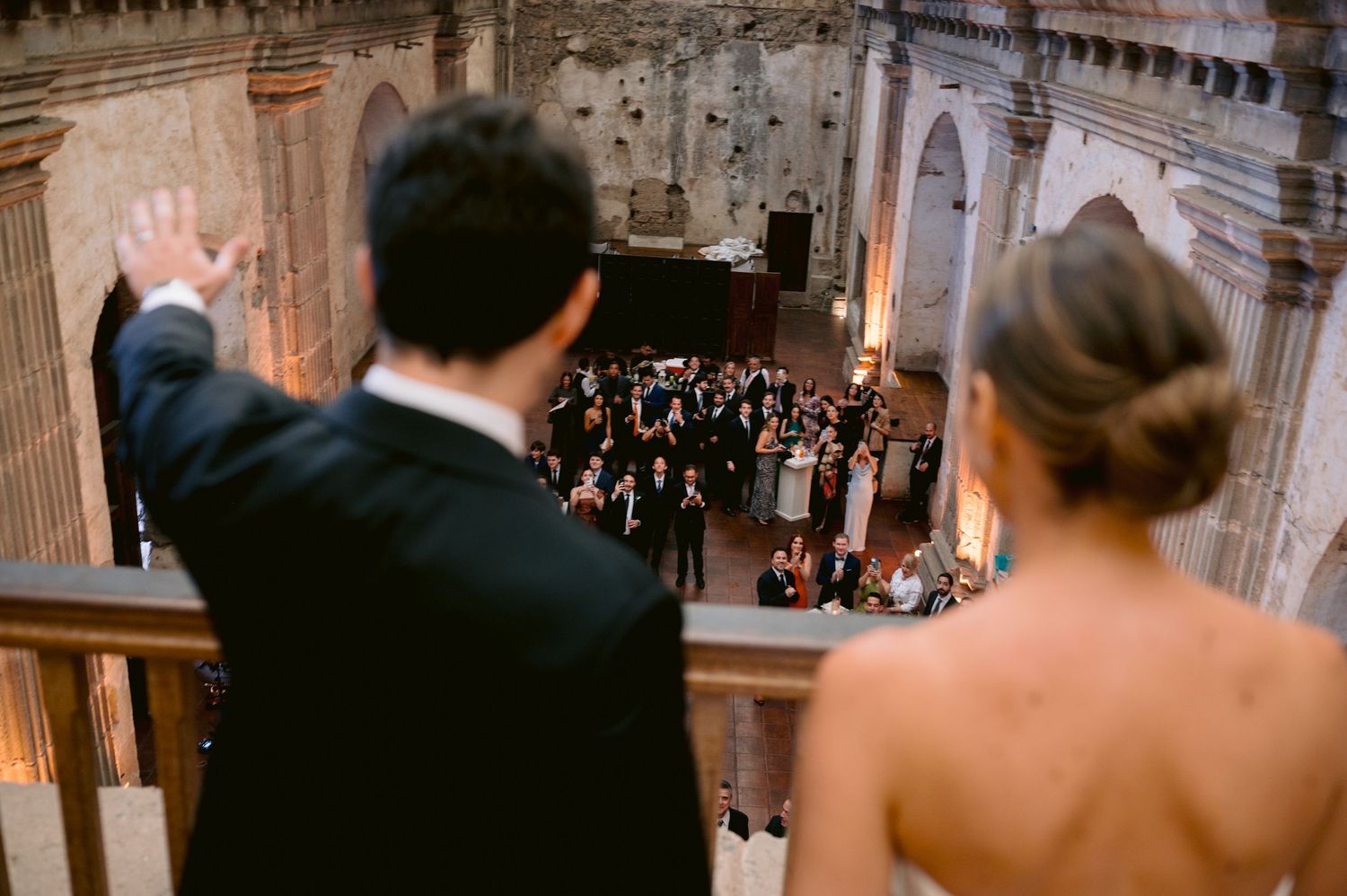 A couple overlooks an orchestra performing in an elegant historic venue from a high balcony.