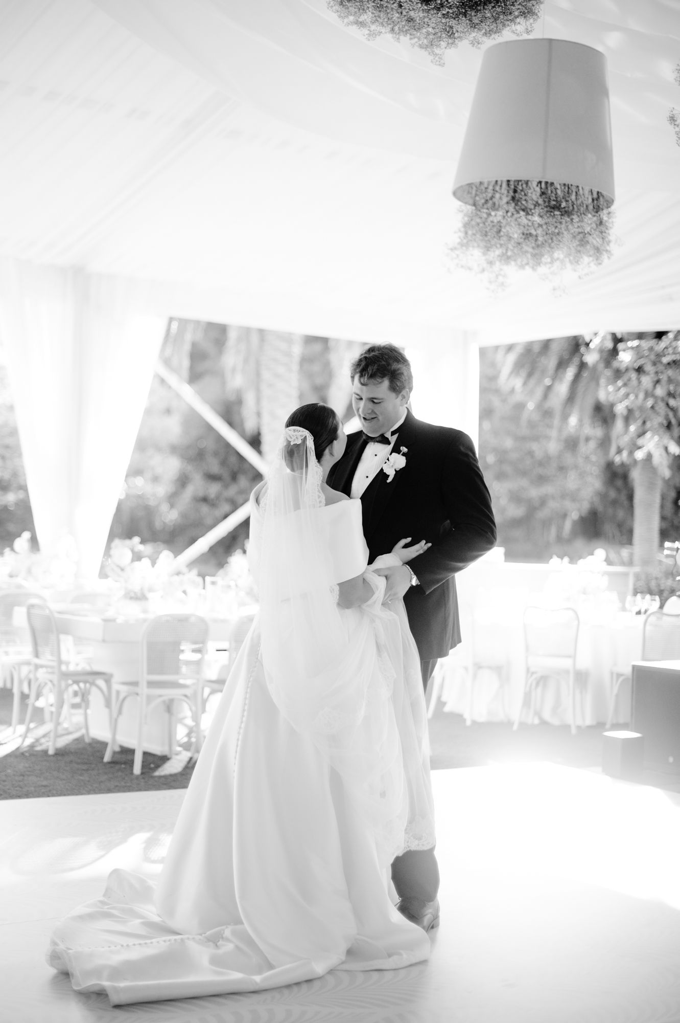 Black and white photo of couple dancing under elegant tent lighting.