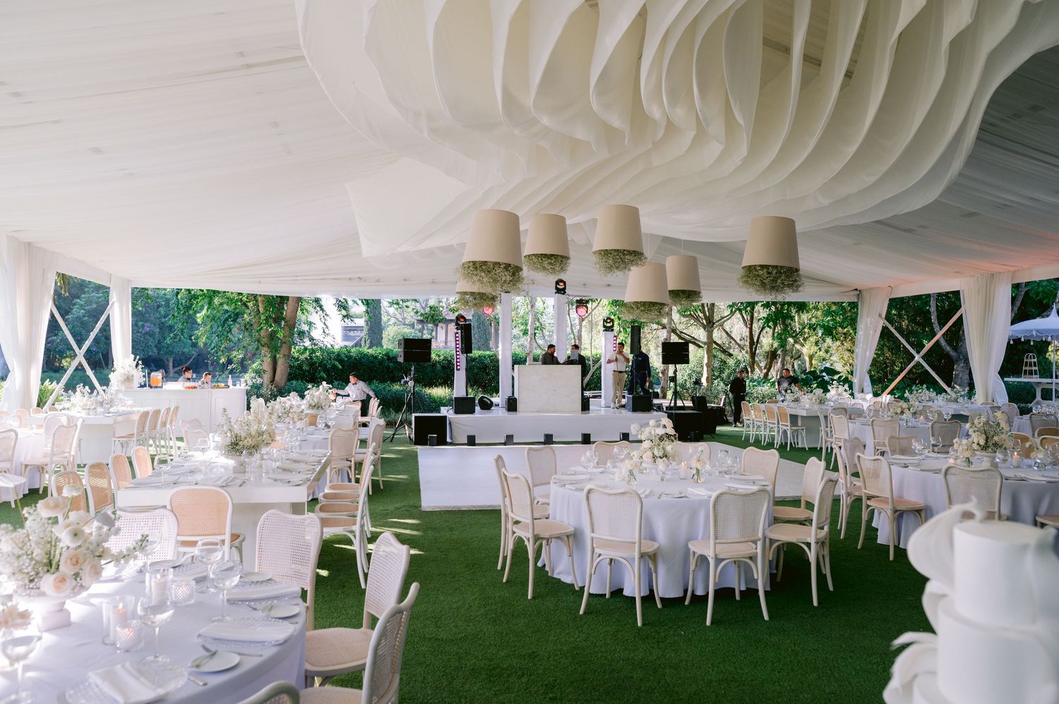Elegant white tent wedding reception setup with round tables and hanging paper lantern decorations.