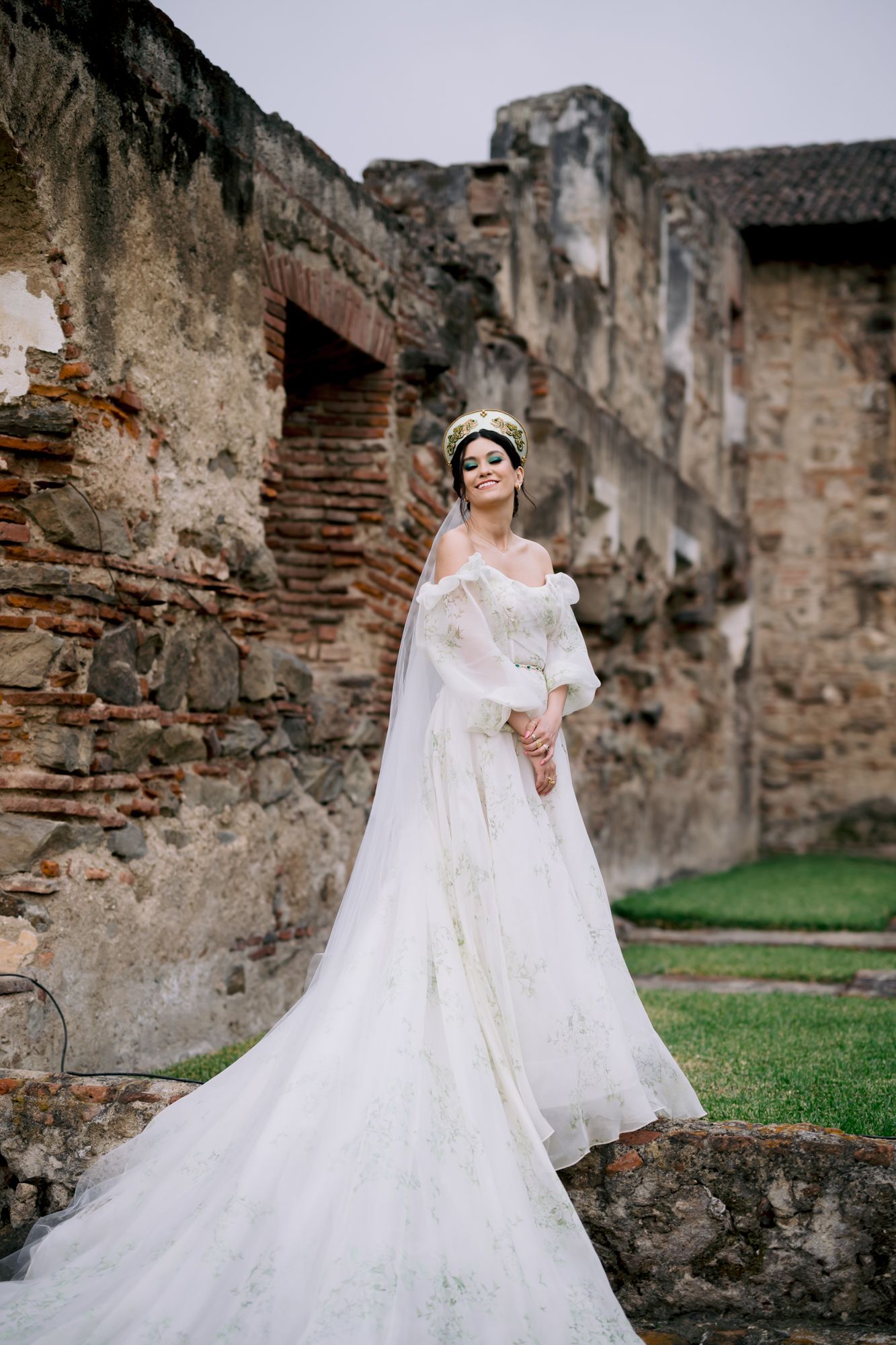 Dramatic full-length bridal portrait featuring flowing train against ancient stone walls.