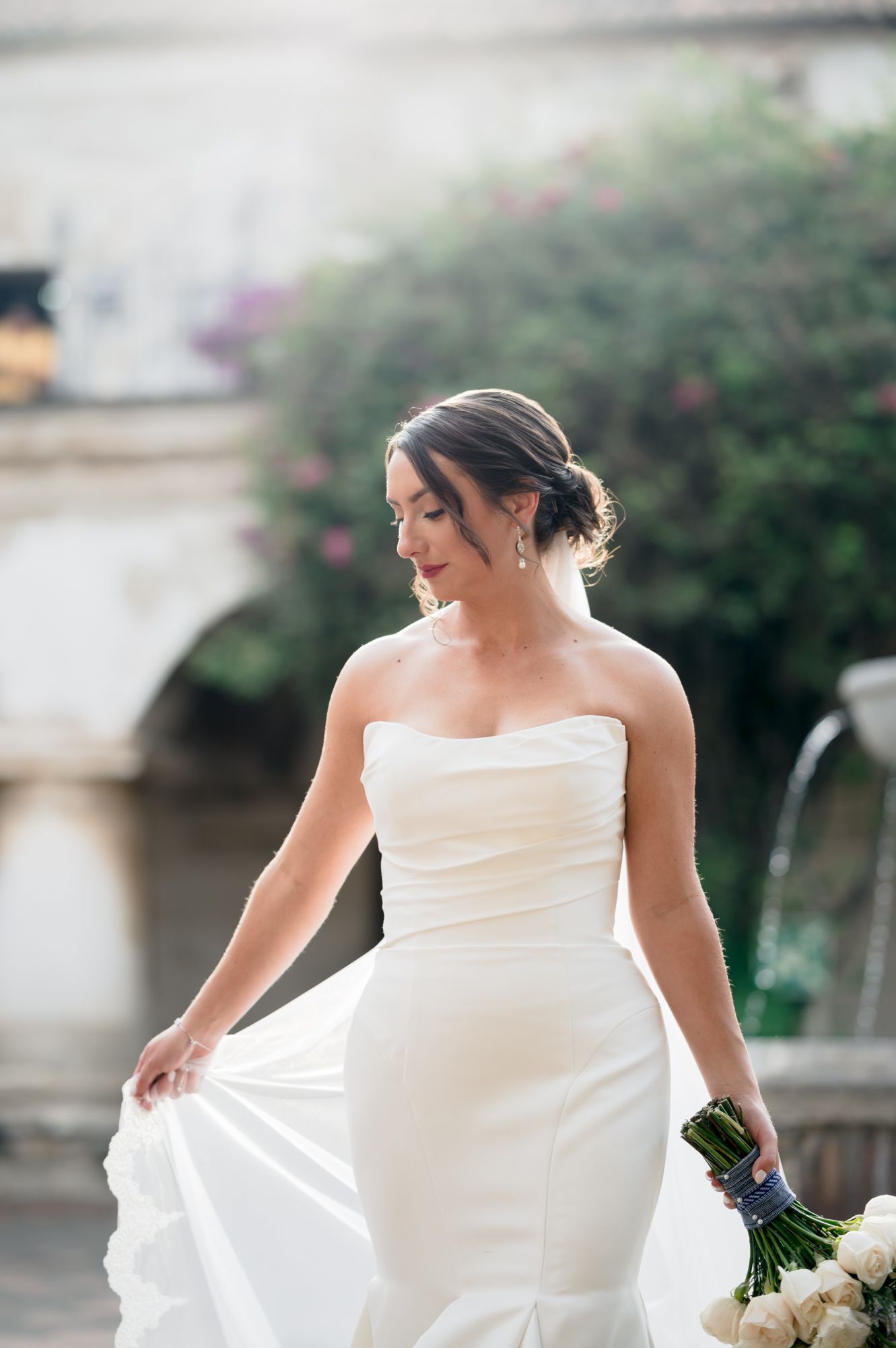 A bride in a strapless white gown twirls her dress in an elegant outdoor setting.