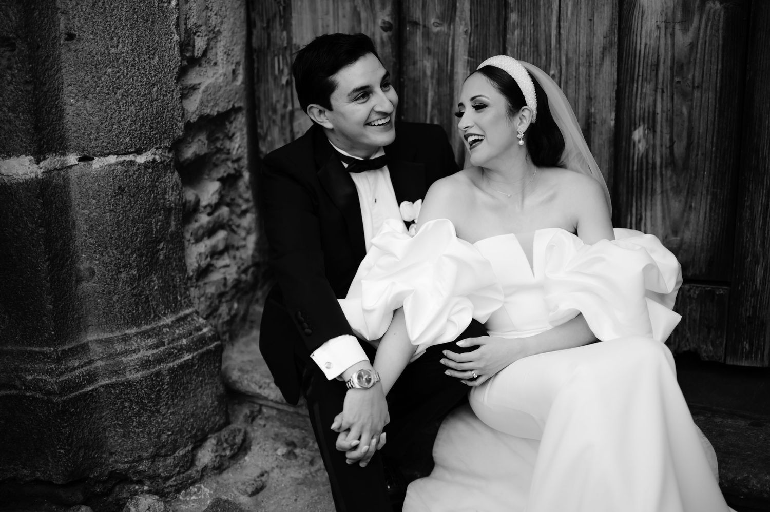 Intimate black and white portrait of wedding couple seated against stone architecture.