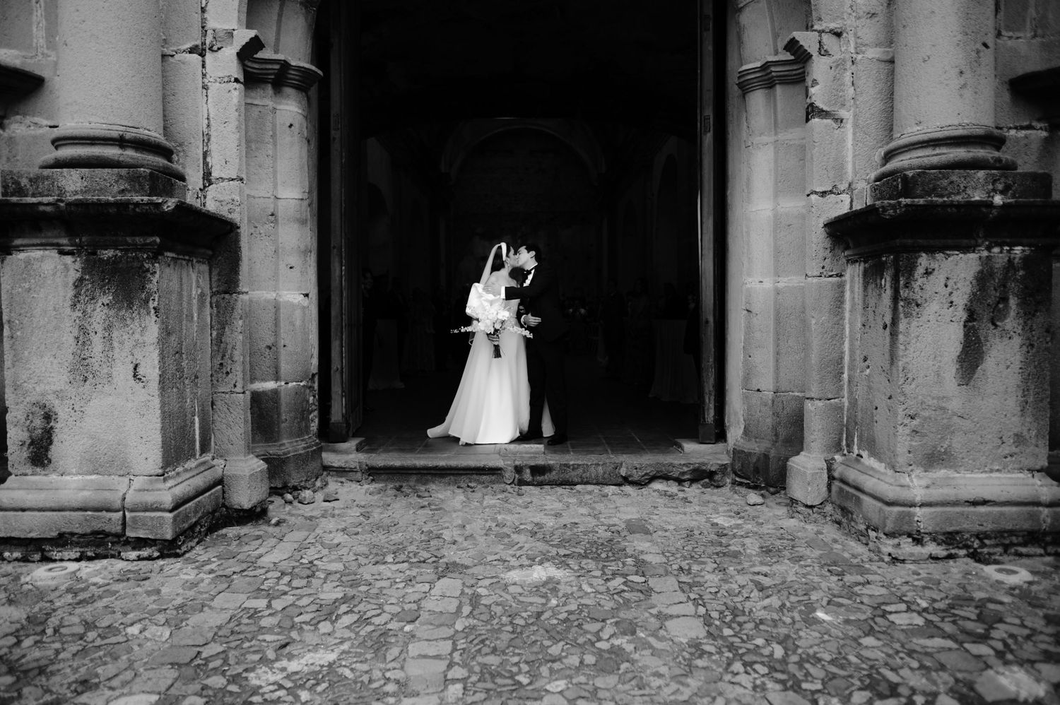 Dramatic black and white wedding portrait framed by historic stone archway.