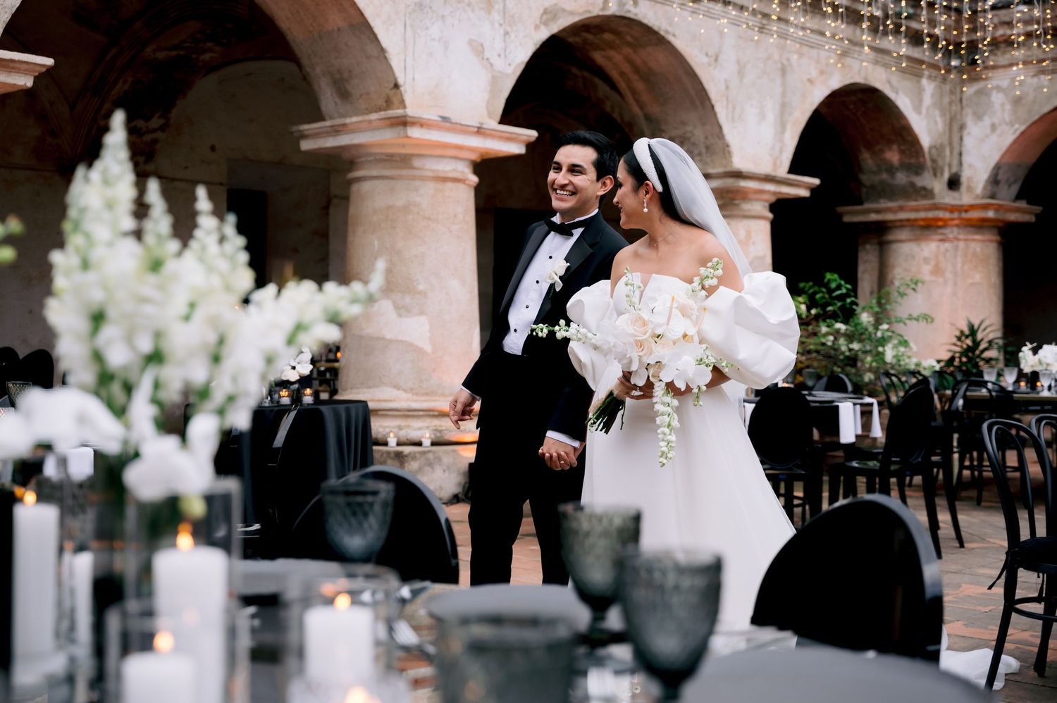Elegant wedding reception under stone arches with classic table settings and floral arrangements.