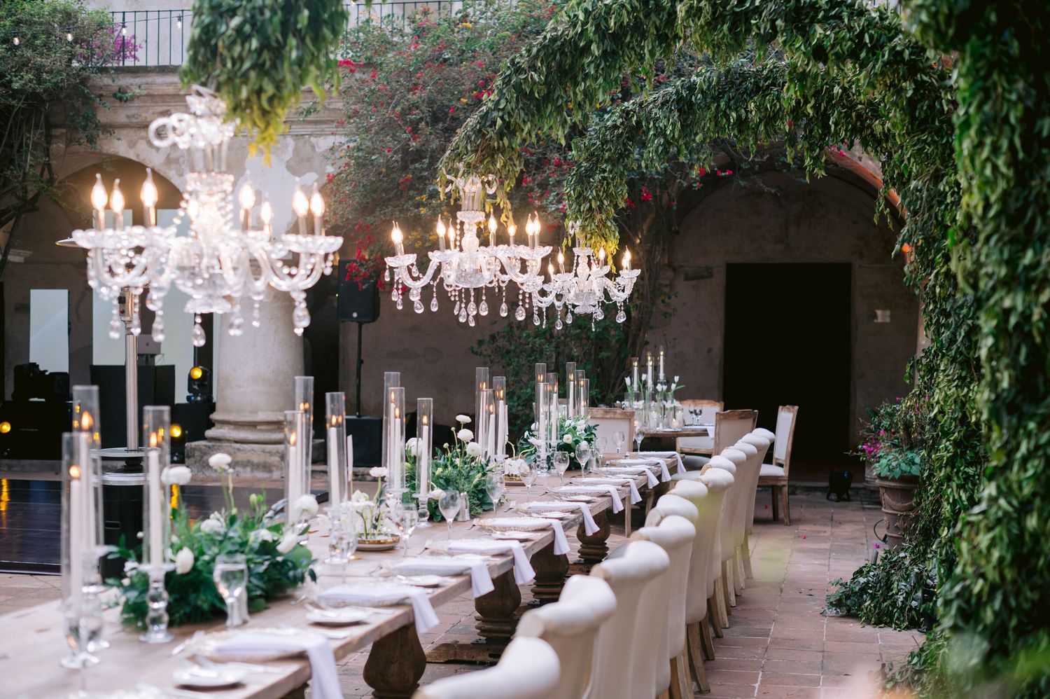 Elegant reception setup with crystal chandeliers and green foliage in historic courtyard.