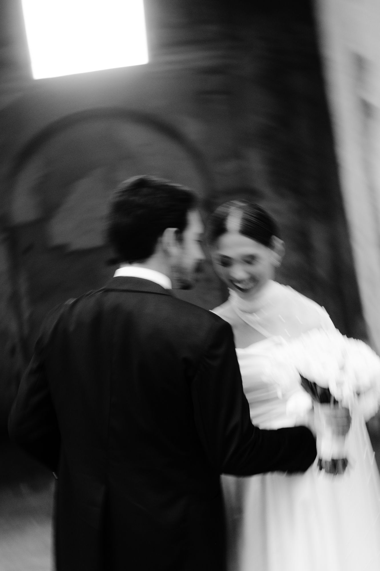 Black and white candid photo of newlyweds sharing an intimate moment with white bouquet.