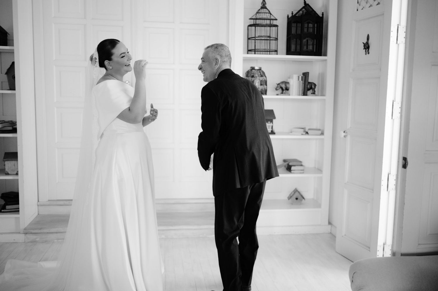 A black and white wedding photo showing a light-hearted exchange in front of built-in shelves.