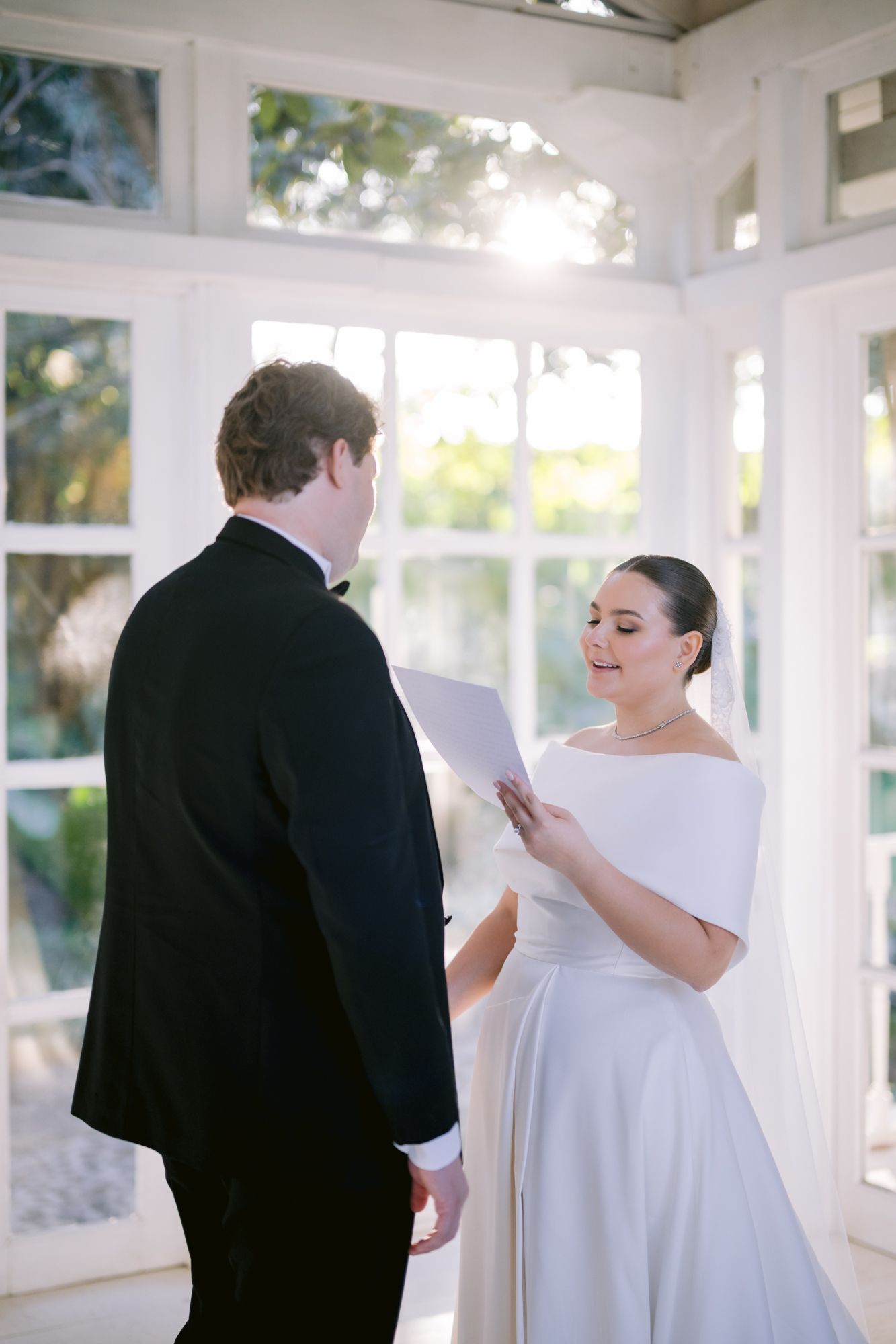 A couple exchanging vows in a bright, white conservatory filled with natural light.