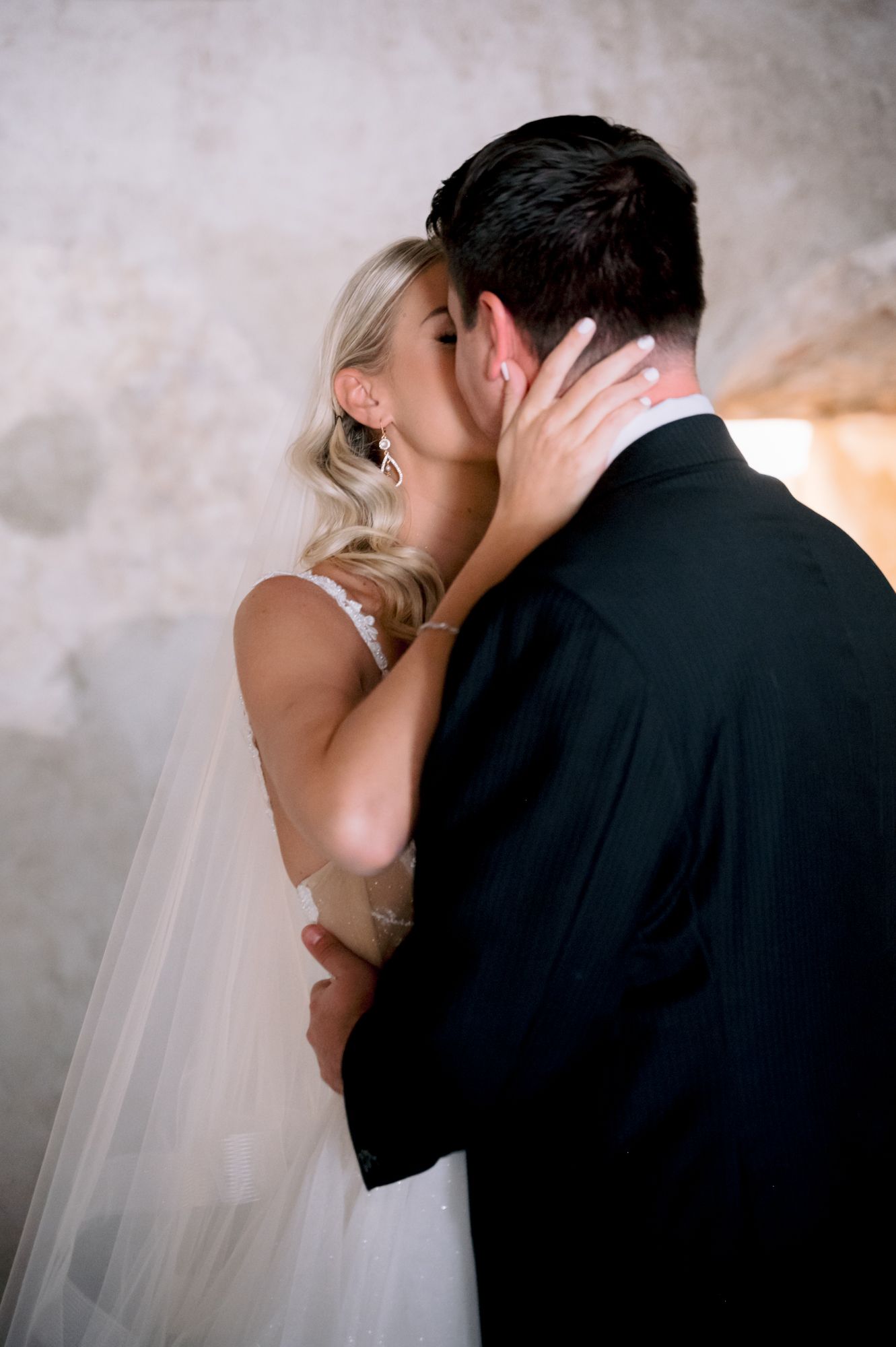 Intimate wedding moment captured as couple shares tender kiss in historic stone venue.