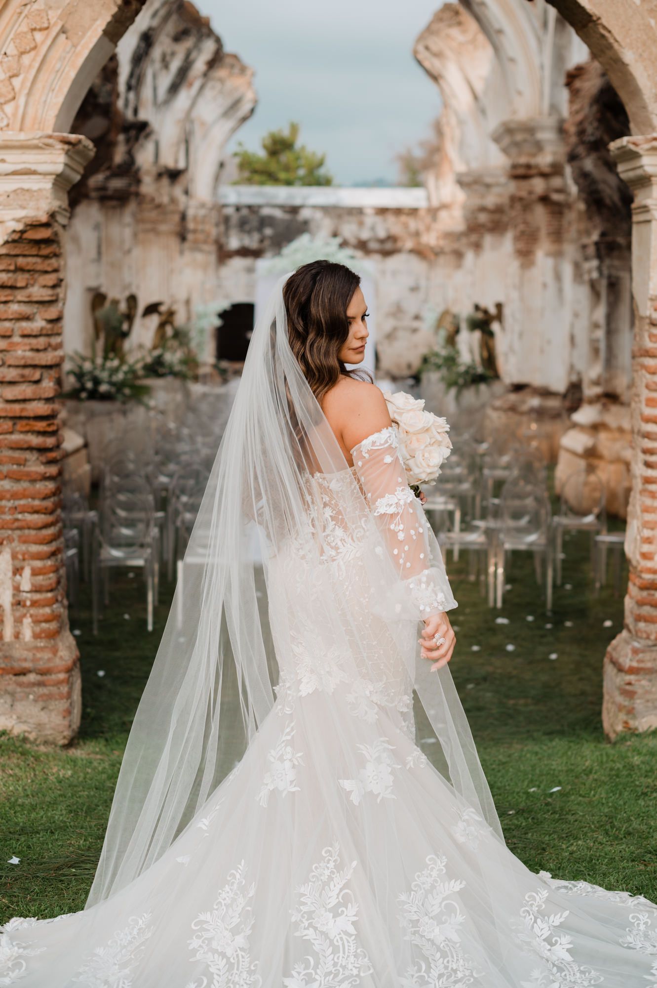 Bride in lace gown poses gracefully among historic brick archways.