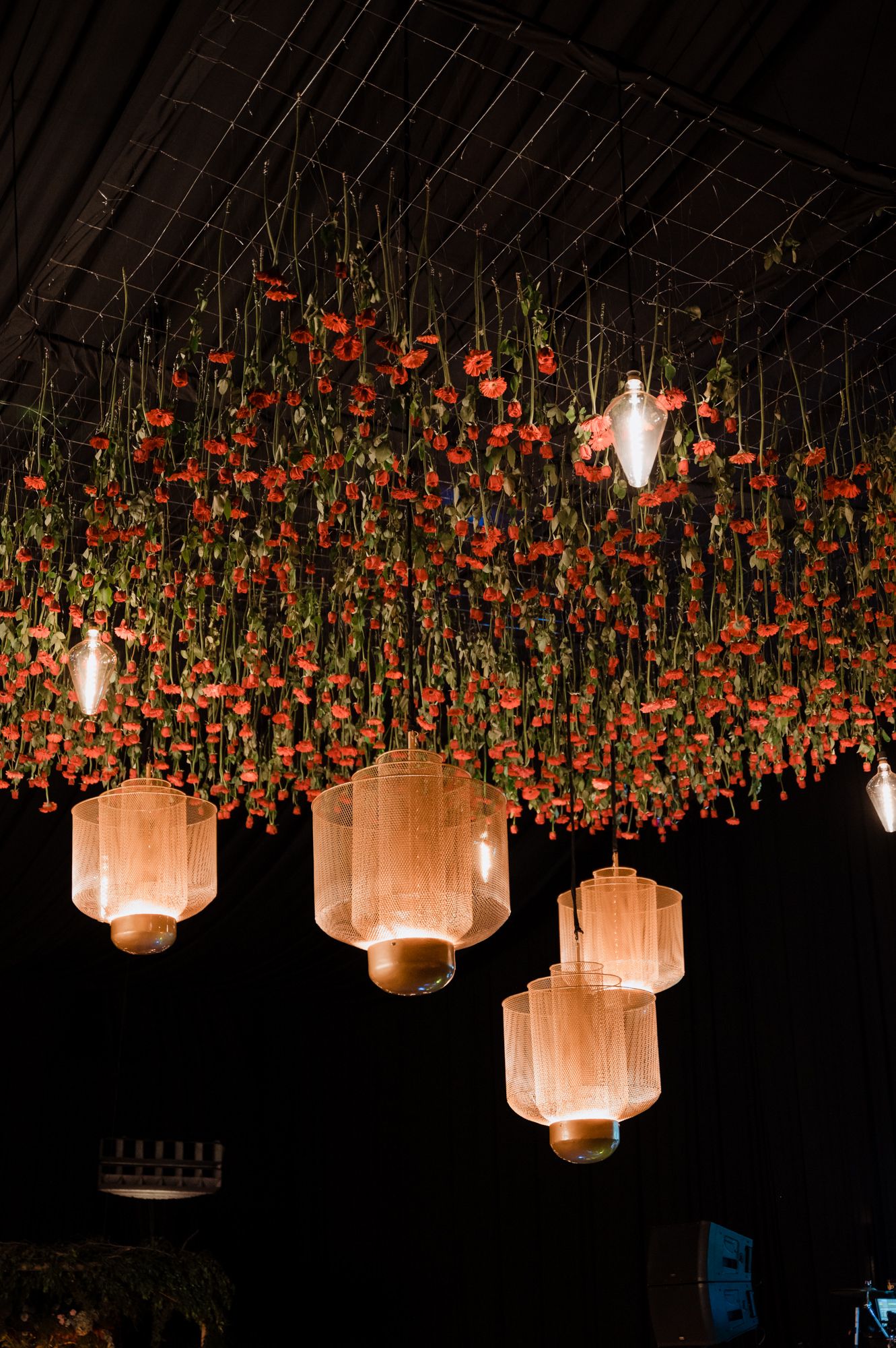 Stunning ceiling installation with hanging red florals and glowing lantern lights creating a magical atmosphere.