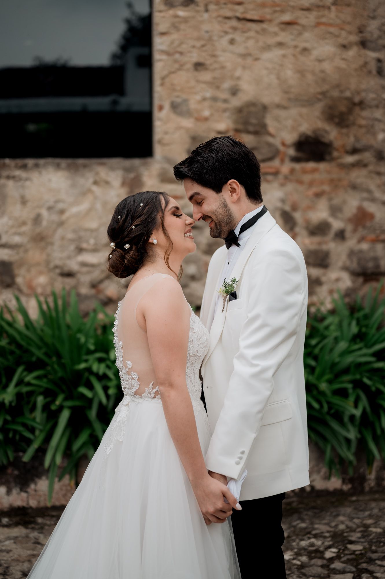 Joyful wedding couple sharing tender moment by stone wall with greenery.