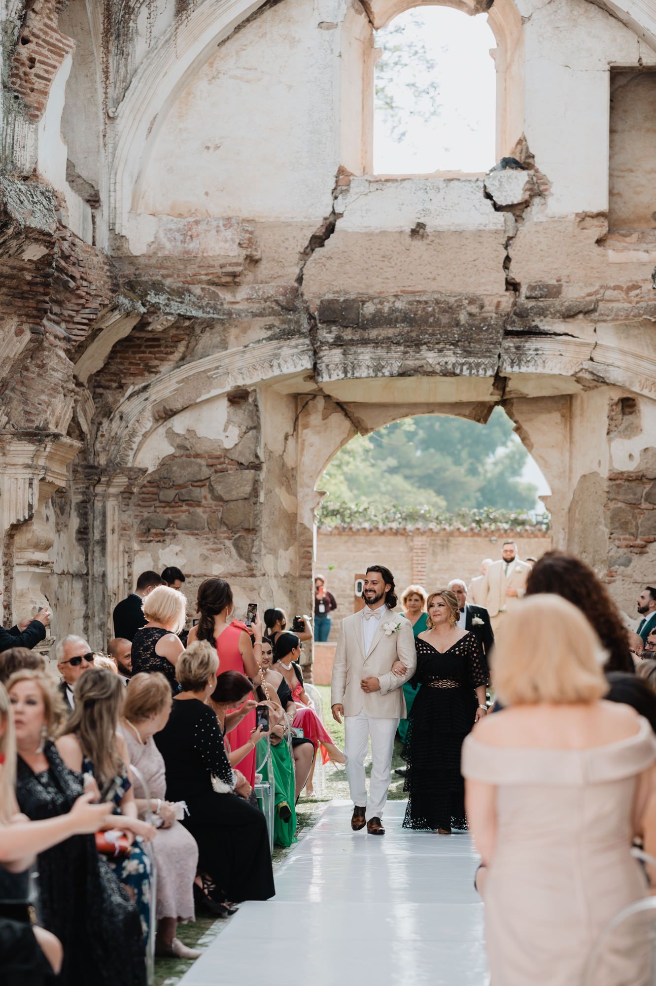 Wedding ceremony takes place in an old stone archway with crumbling walls and guests seated on both sides.