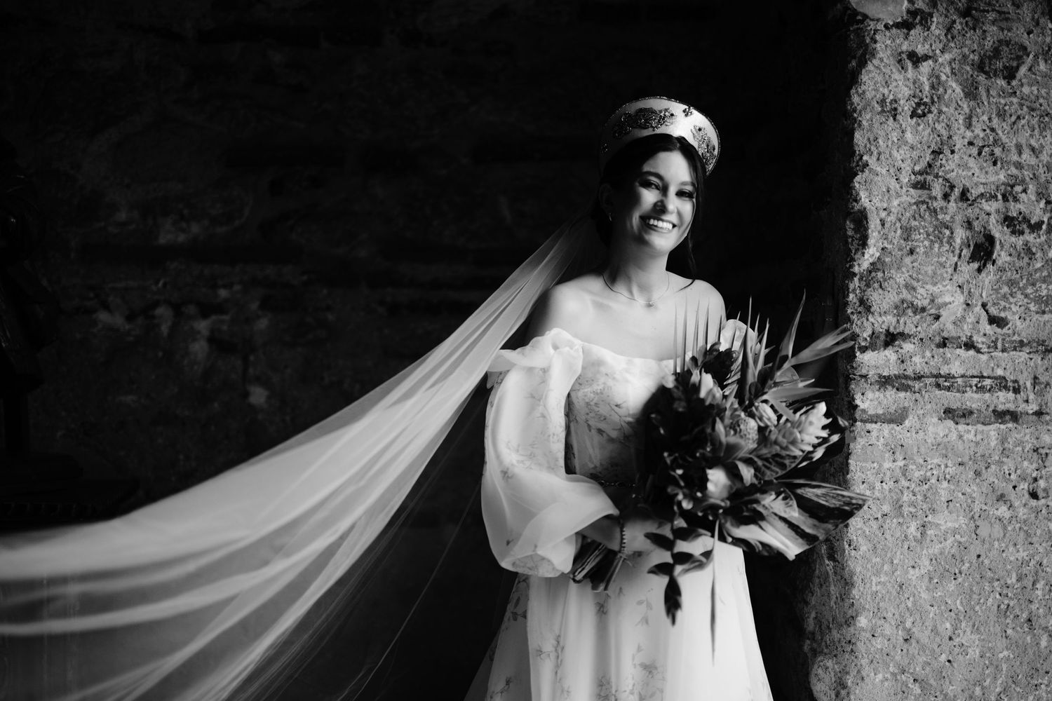 Black and white portrait of bride with flowing veil holding colorful wedding bouquet.