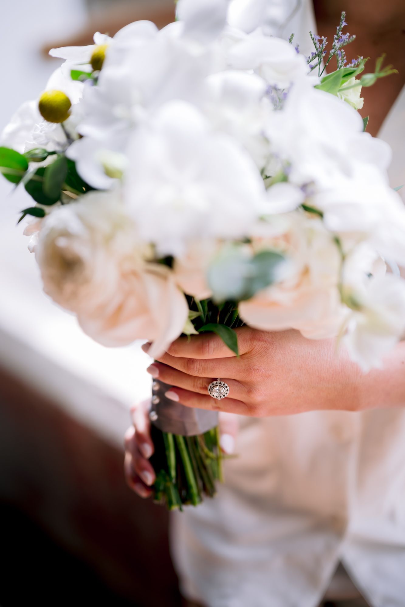 A close-up of a bridal bouquet with white flowers and a diamond engagement ring.