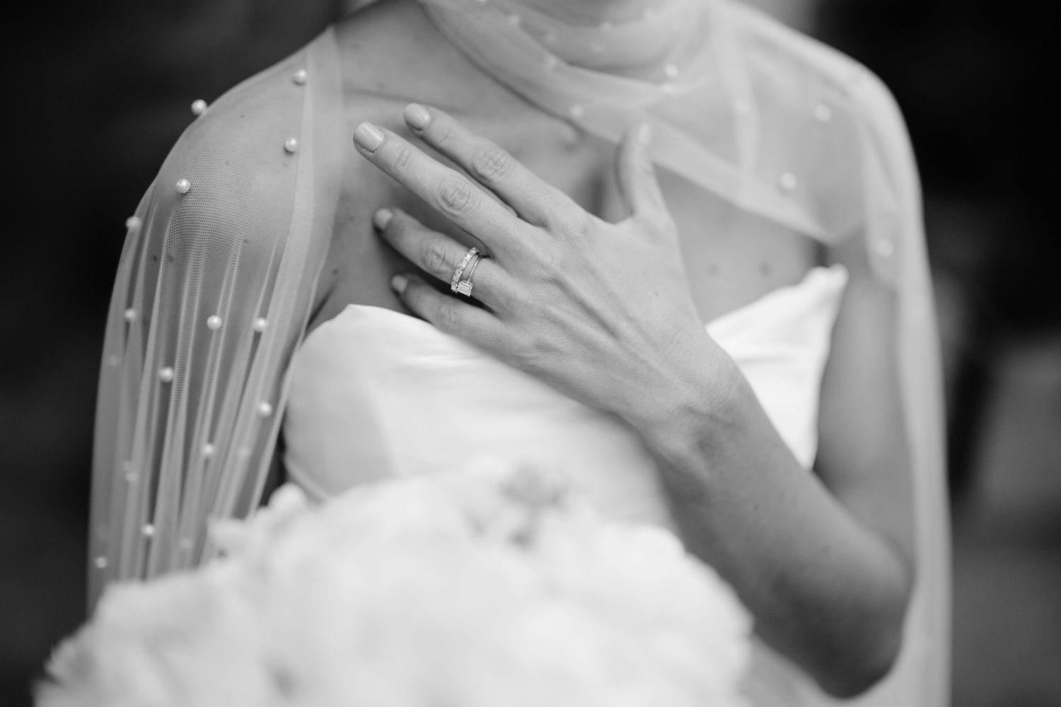 Black and white detail shot of pearl-adorned bridal cape and wedding ring.