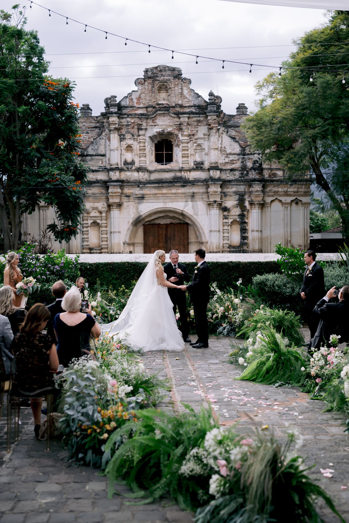 Outdoor wedding ceremony with elegant floral arrangements lining stone path leading to historic church facade.