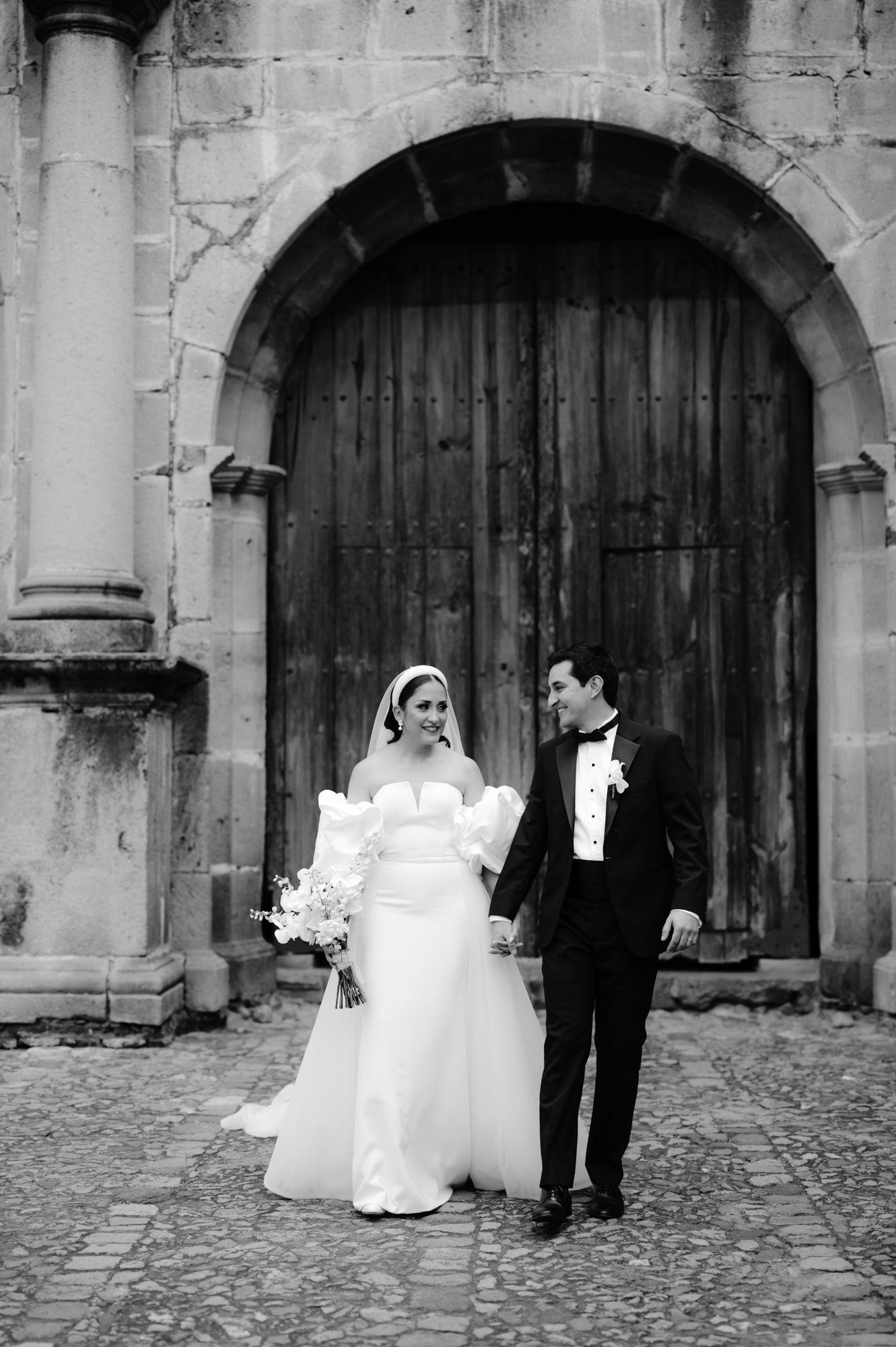Elegant wedding couple poses before grand wooden cathedral door.