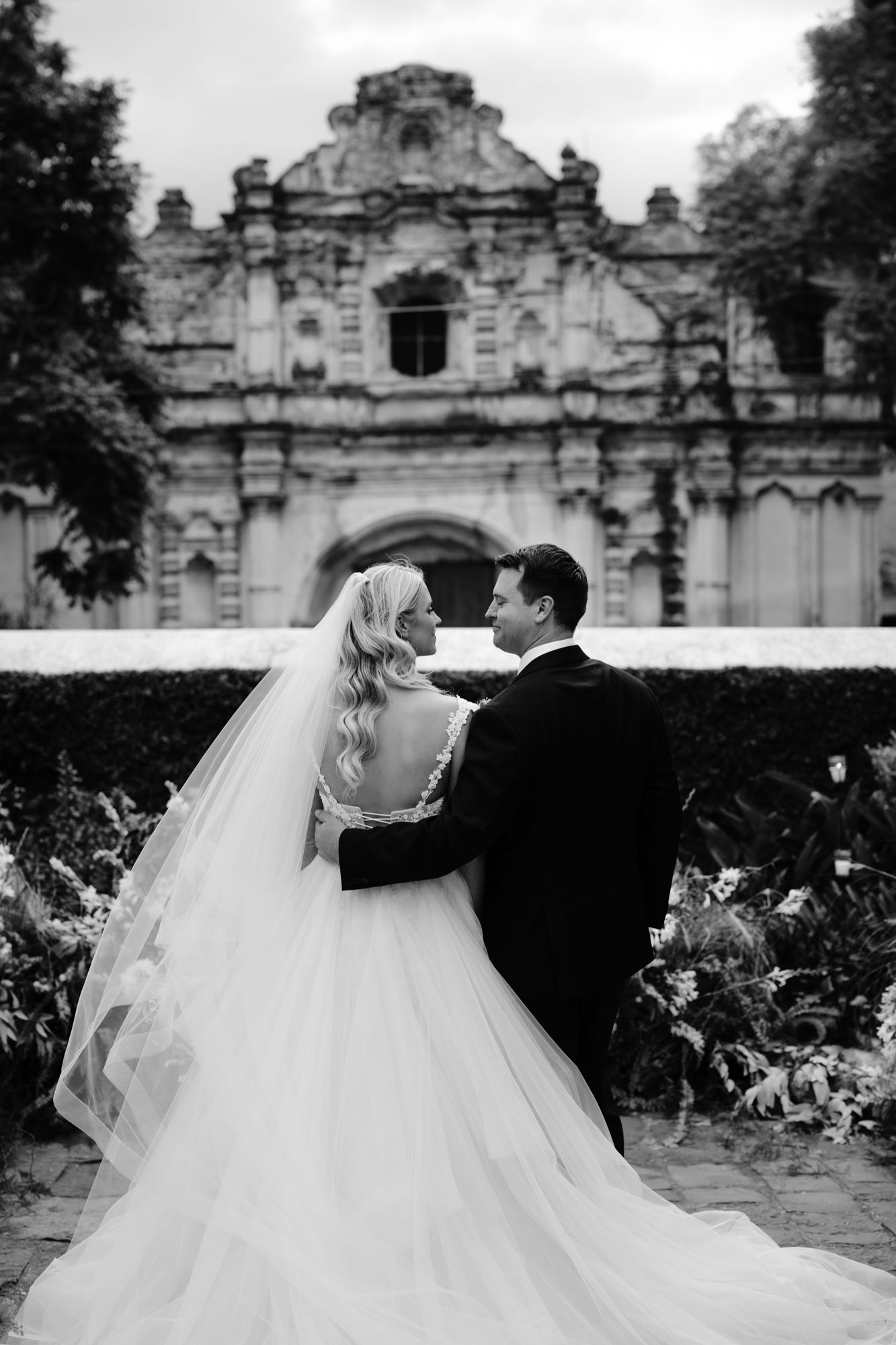 Black and white wedding portrait with a classic embrace in front of historic architecture.
