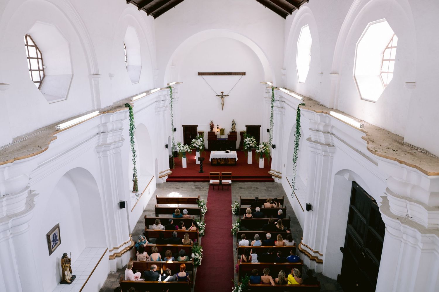 Interior view of a white church sanctuary with wooden pews and red carpet leading to the altar.
