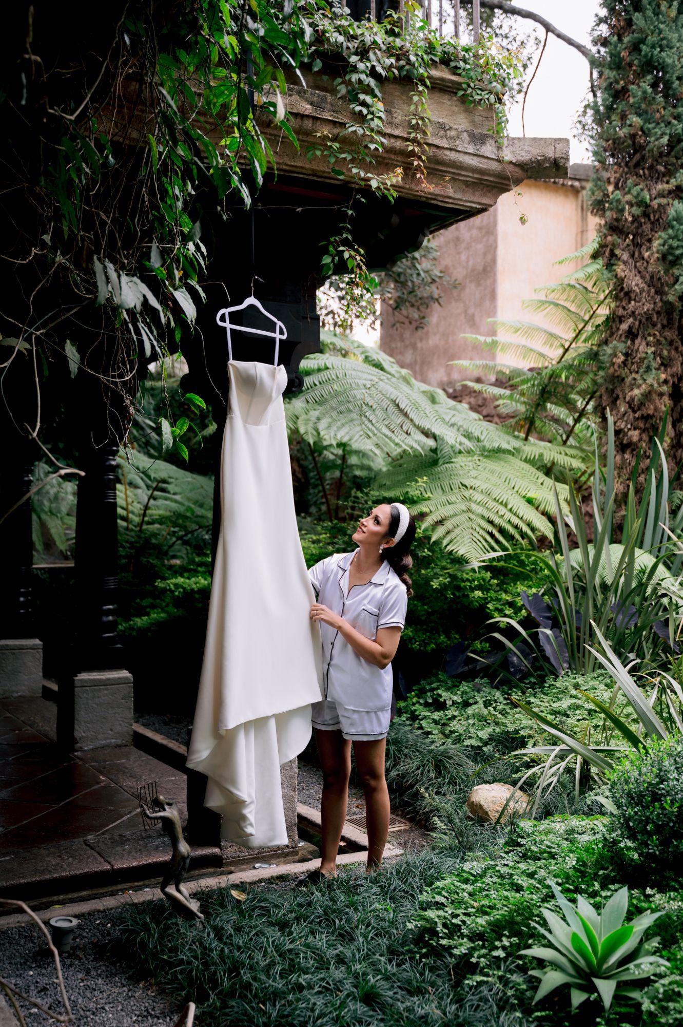 White wedding gown hangs elegantly against lush tropical foliage in an outdoor setting.