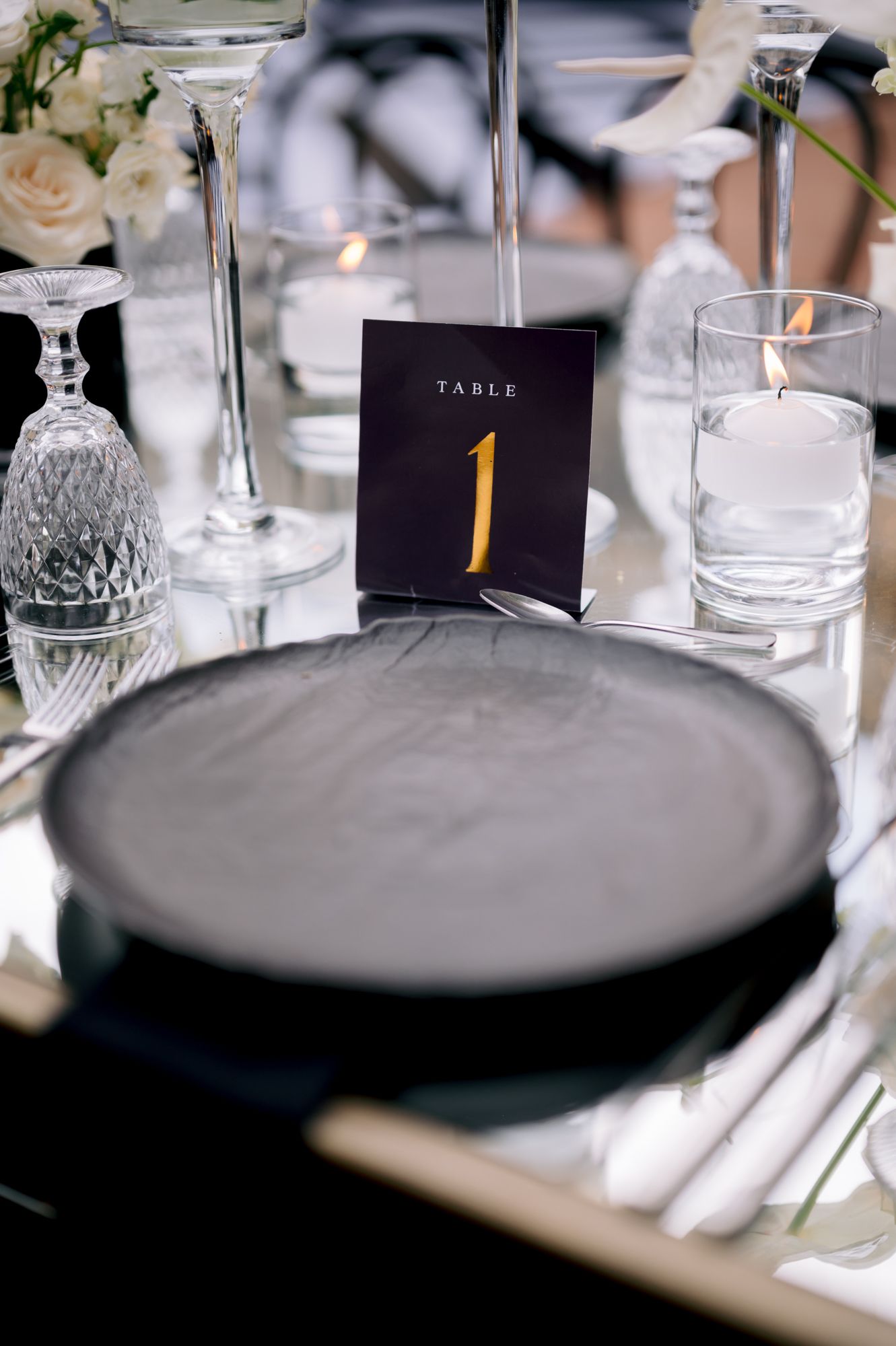 Elegant table setting with black plate, crystal glassware and gold table number one card at wedding reception.