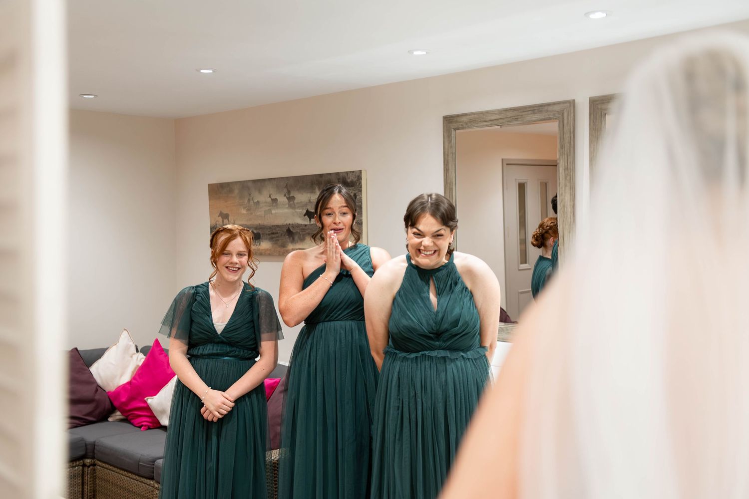Bridesmaids in emerald green dresses react with joy and excitement as bride reveals her wedding gown.