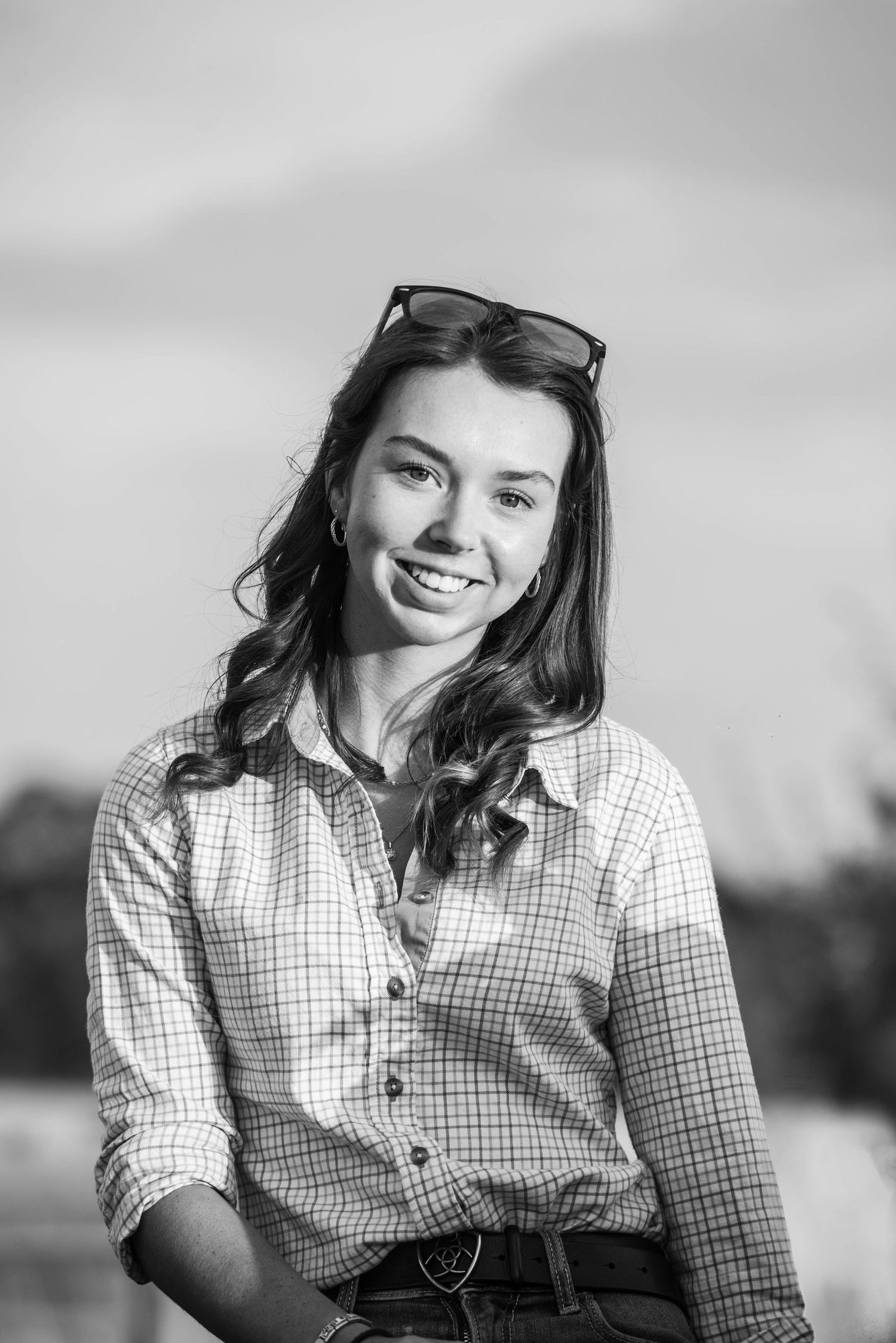 Black and white portrait of a smiling young woman with sunglasses on her head outdoors.
