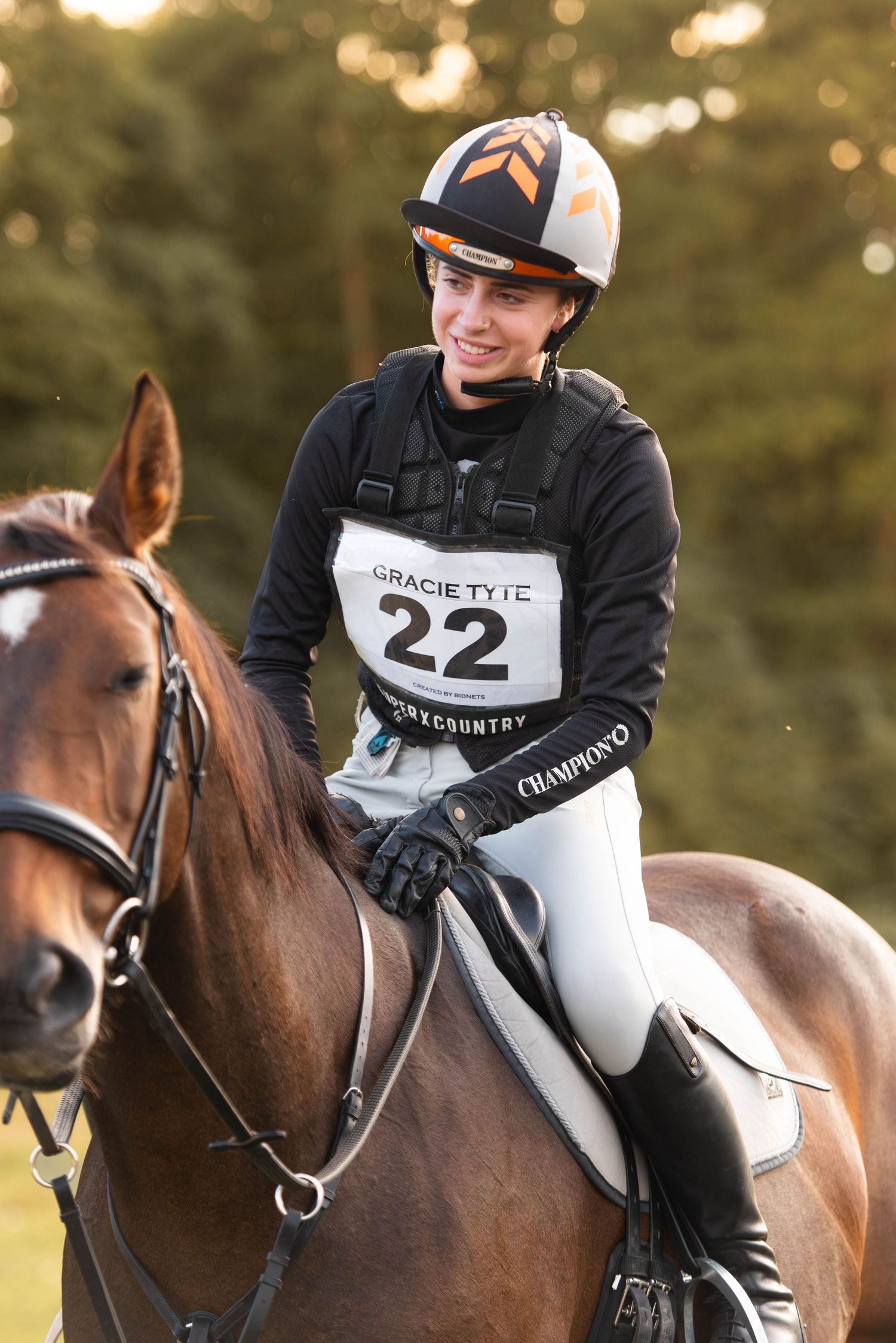 Smiling equestrian competitor number 22 Gracie Tyte riding a chestnut horse at a cross-country event.