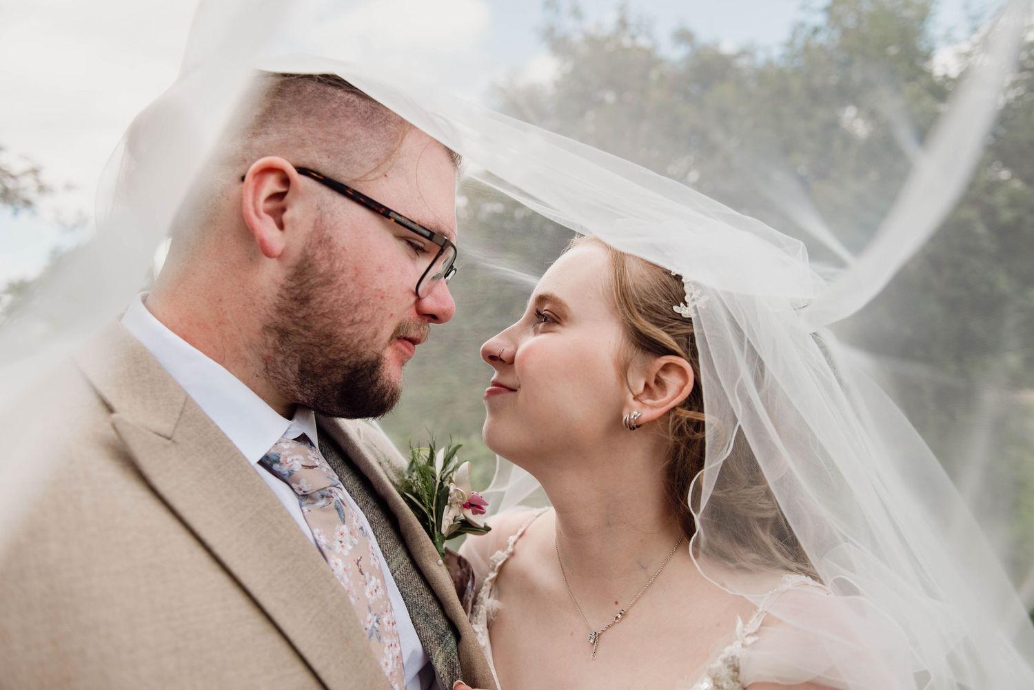 Bride and groom share a romantic moment under a flowing veil outdoors on their wedding day.