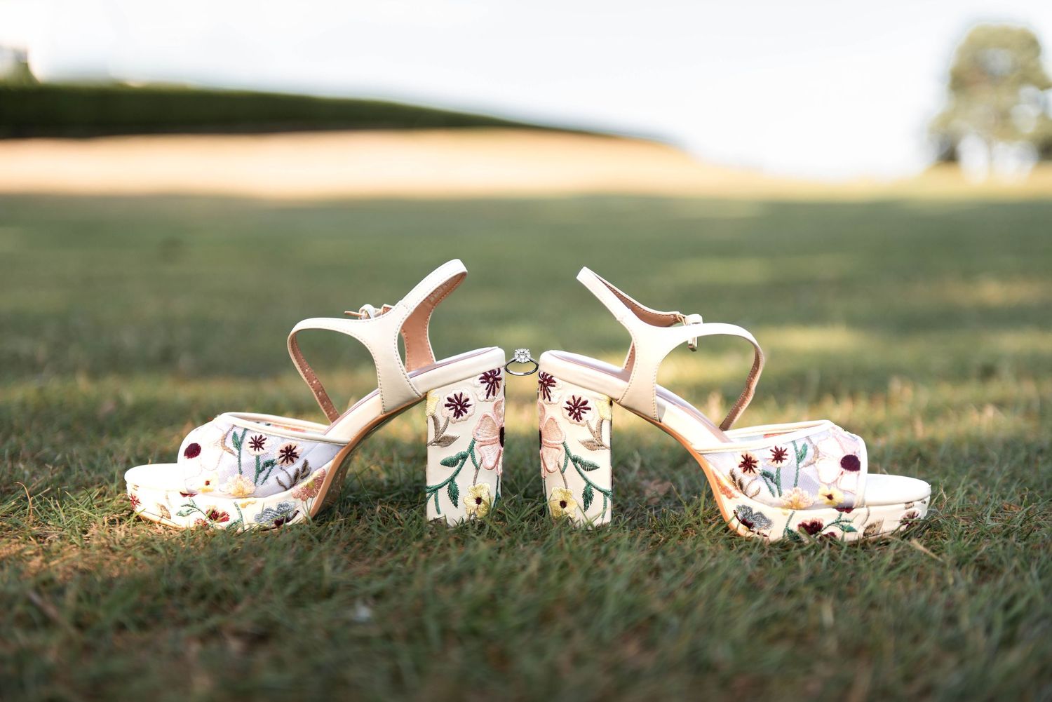 Floral embroidered platform heels with ankle straps displayed on green grass at an outdoor wedding venue.