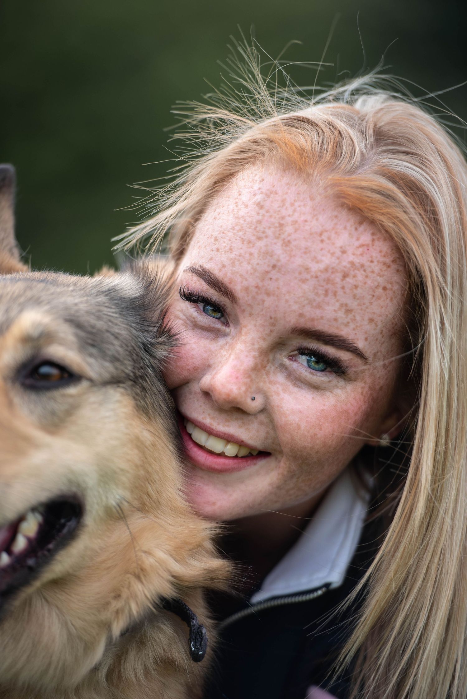 Smiling freckled blonde girl with blue eyes posing closely with her German Shepherd mix dog.
