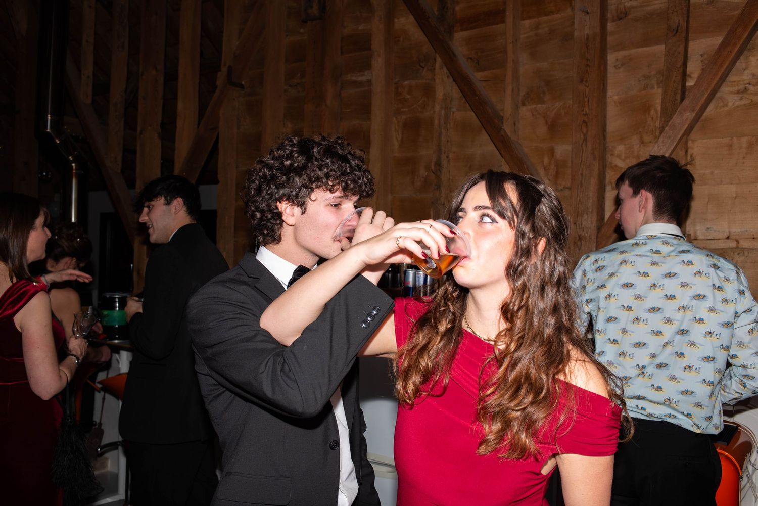 Young couple sharing a drink at a formal party in a rustic barn venue.