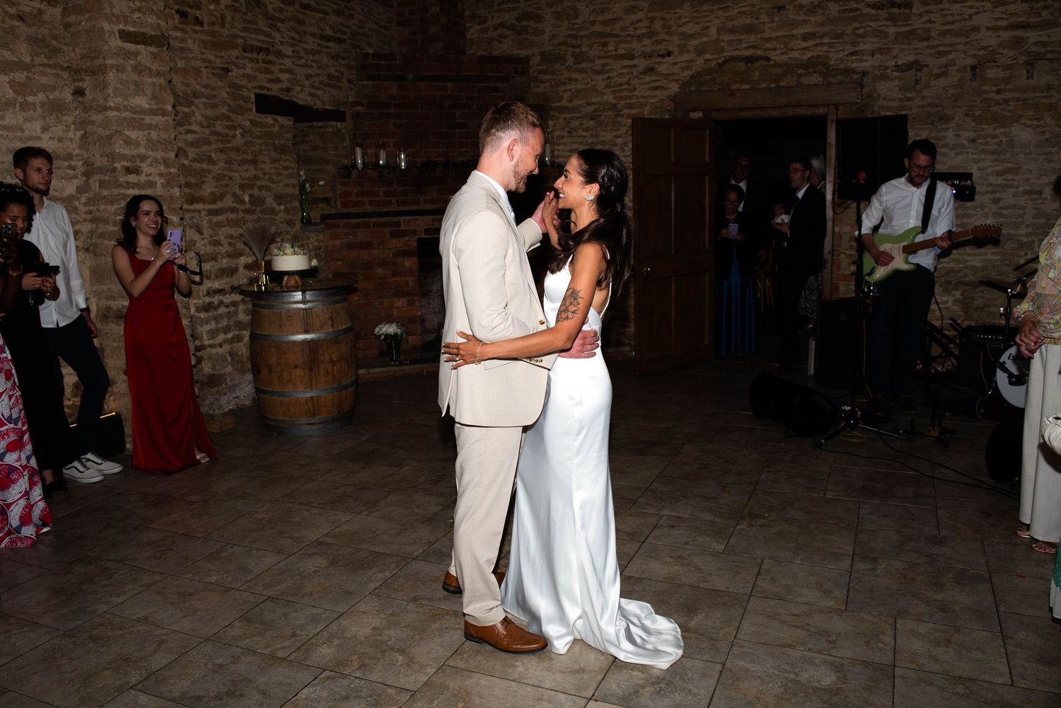 Bride and groom sharing their first dance in a rustic stone barn venue with live band and guests watching.