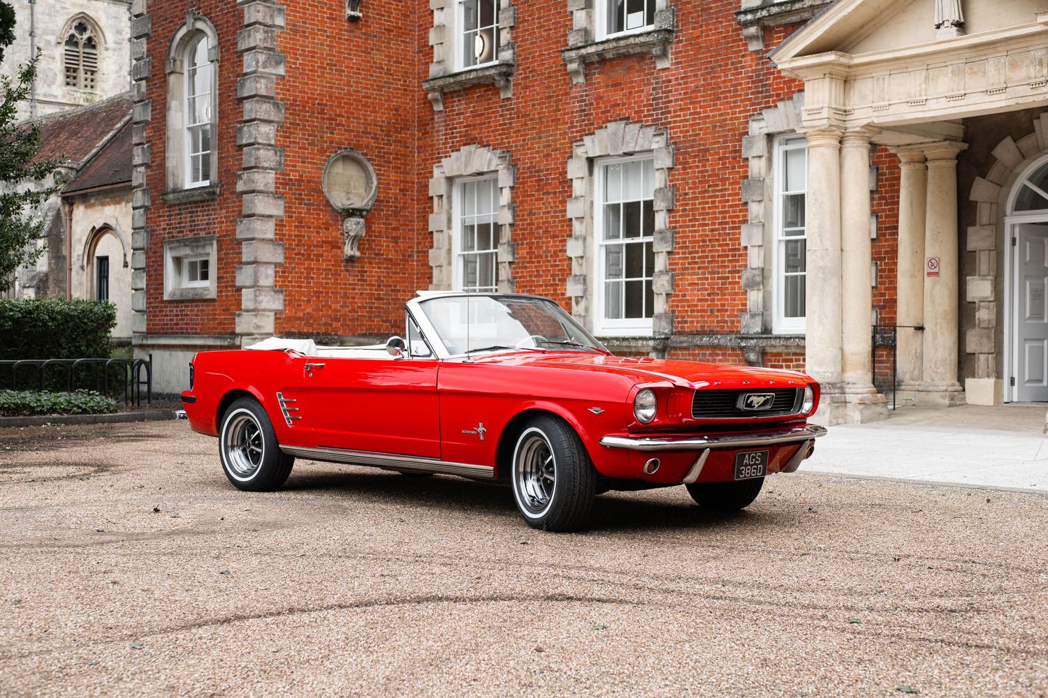 Stunning red Ford Mustang convertible parked in front of a grand historic brick mansion.