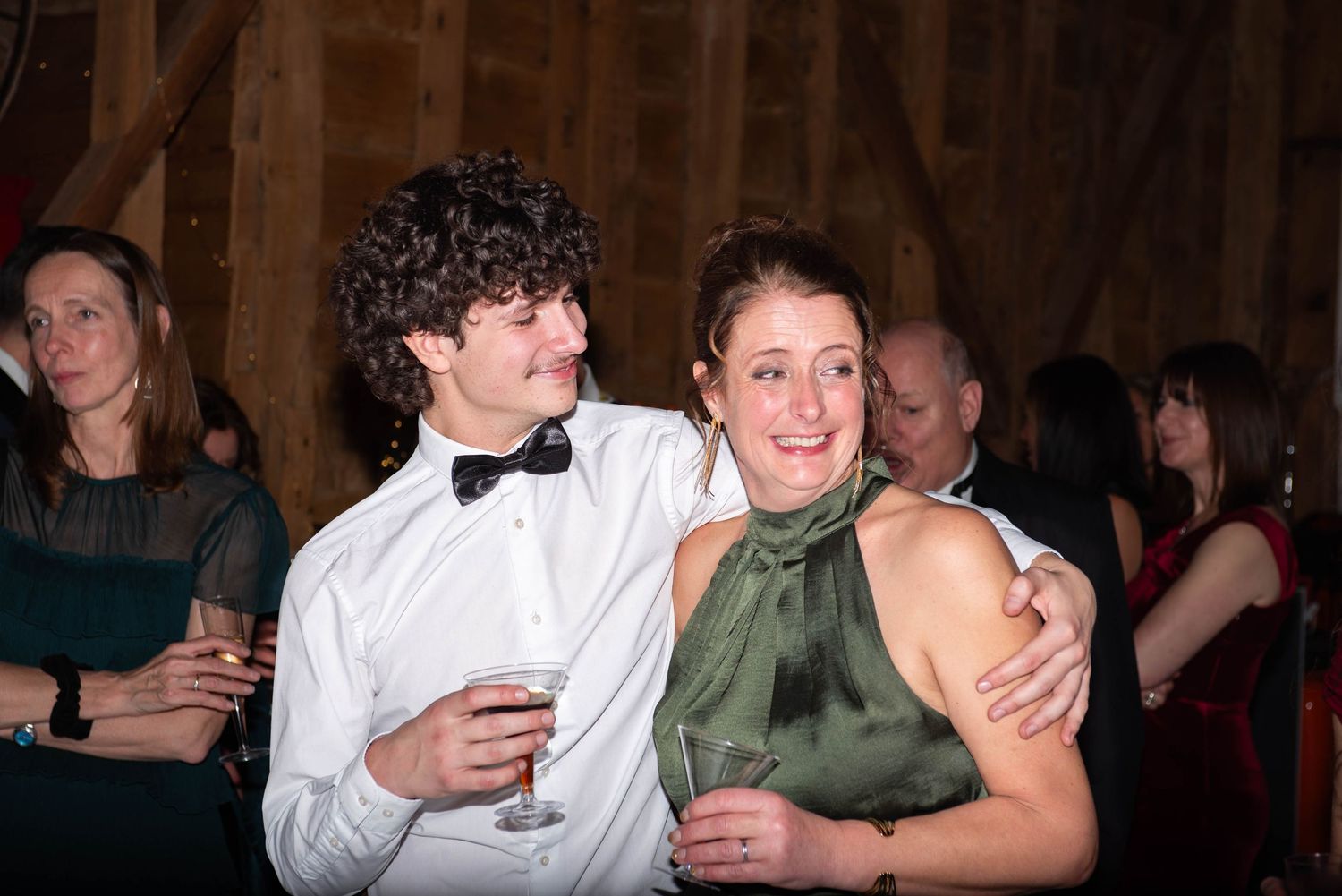 Young man in white shirt embracing woman in green dress at indoor party event.