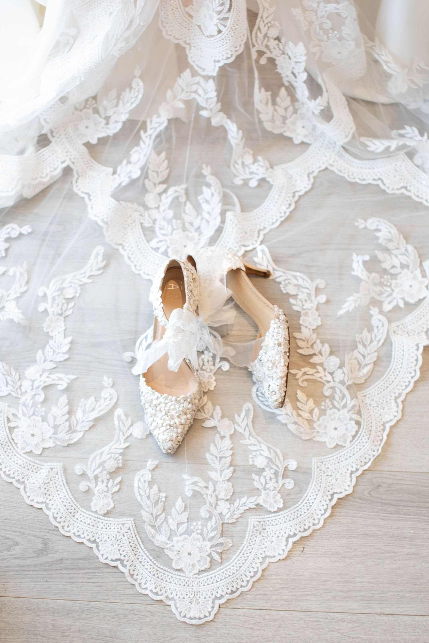 Elegant bridal shoes with floral details resting on lace wedding dress train.