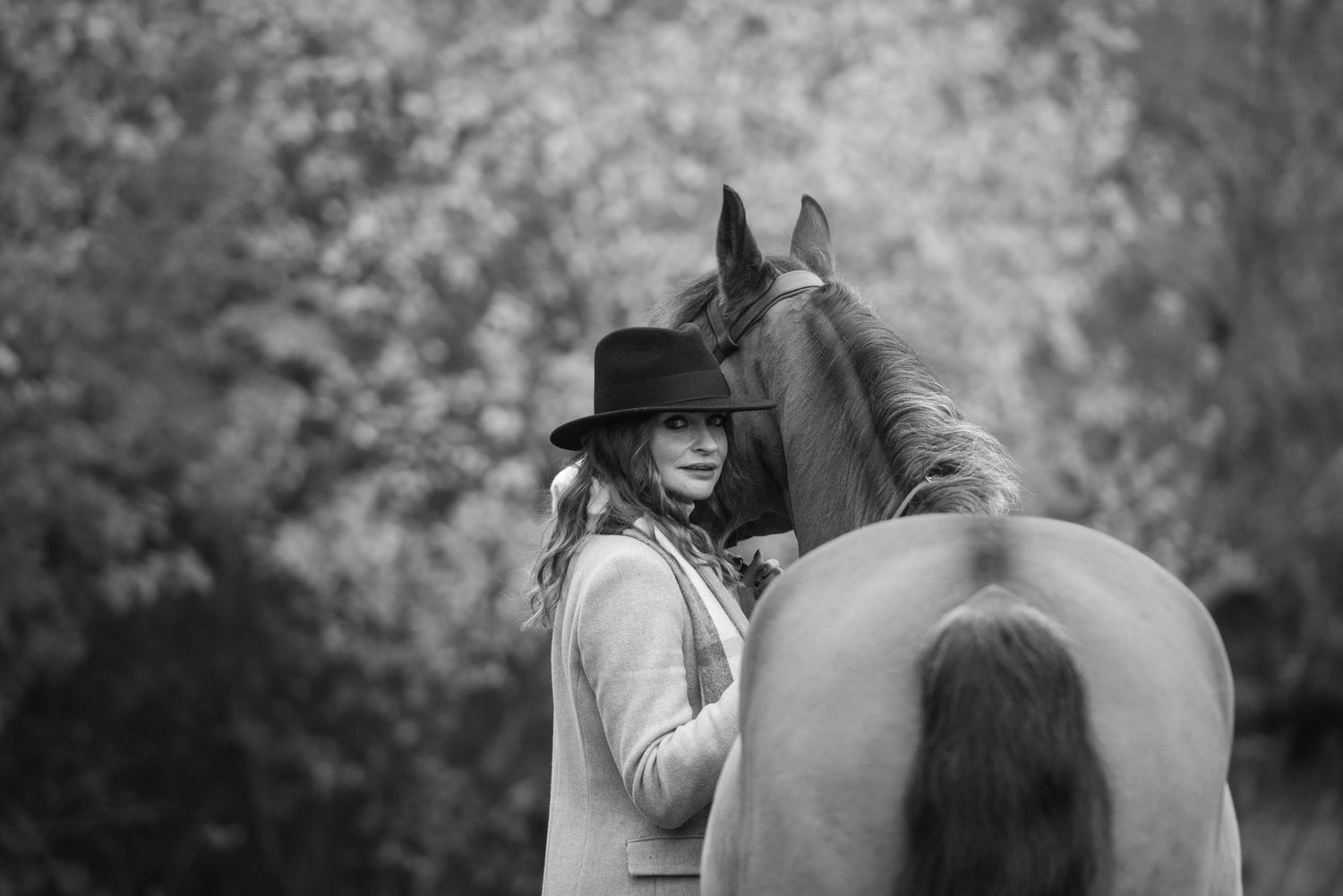 Black and white image of a woman in a wide-brim hat posing closely with a chestnut horse.