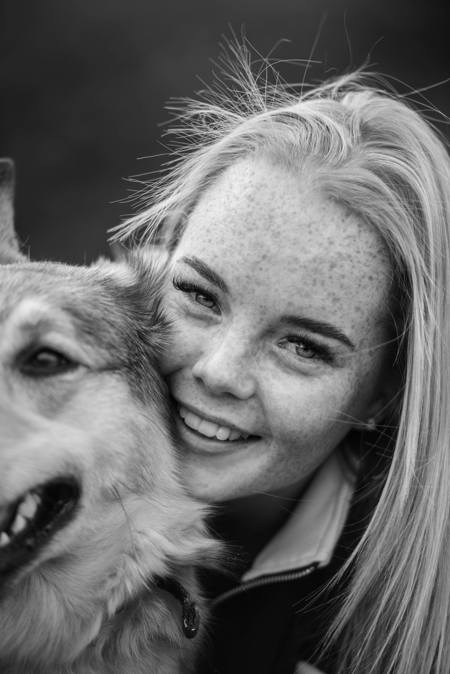 Black and white portrait of a freckled blonde girl smiling cheek-to-cheek with her dog.