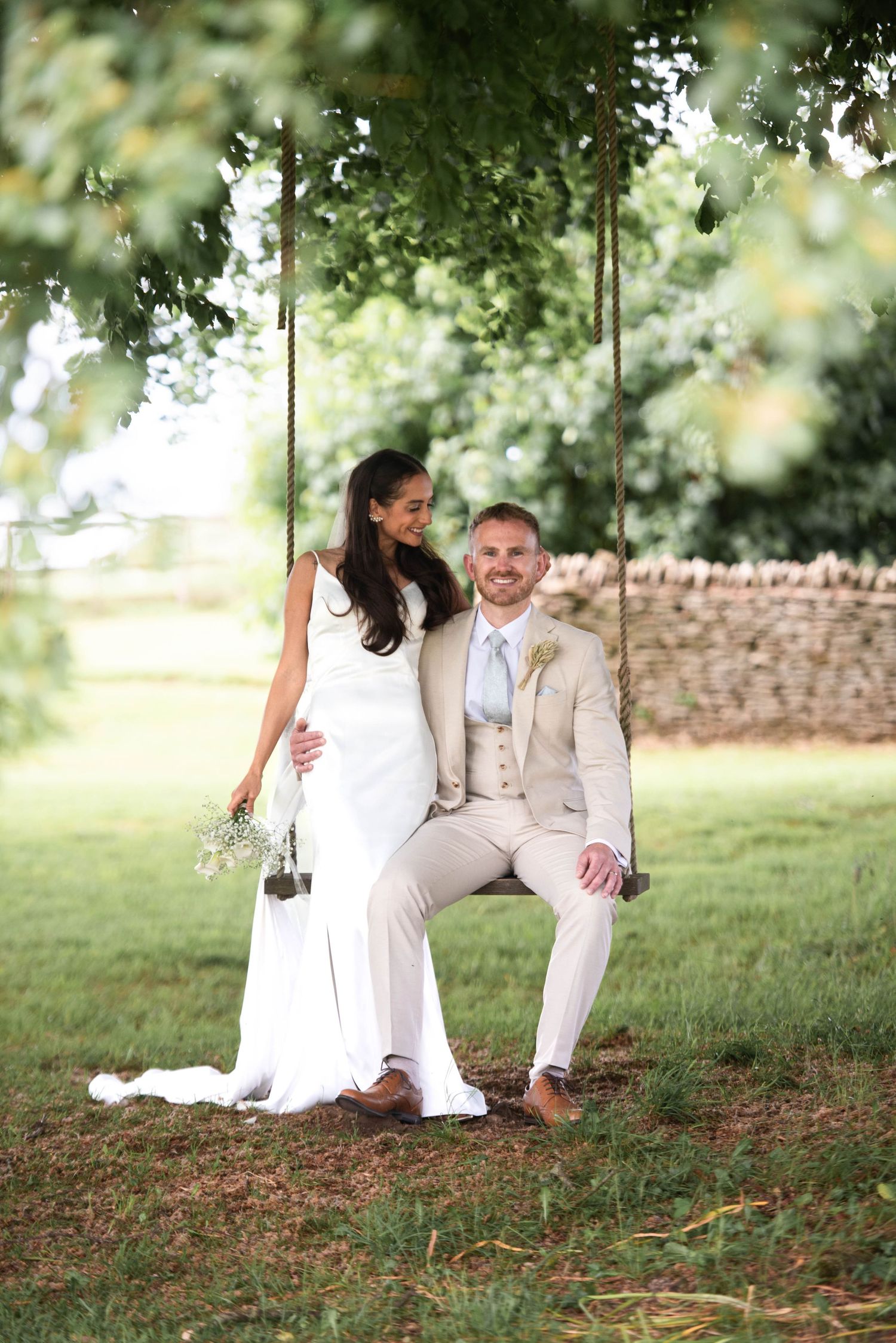 Bride and groom sharing a romantic moment on a wooden swing under a lush green tree.