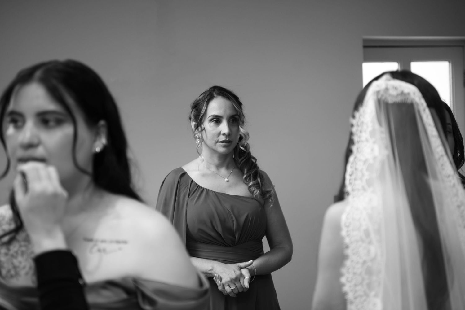 Black and white photo of a bridesmaid watching the bride getting ready in a bridal suite.