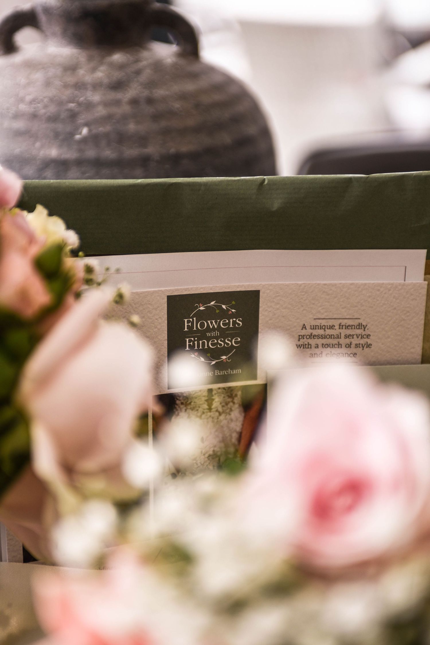 Close-up of Flowers with Finesse floral brochure surrounded by soft pink roses and wedding decor.