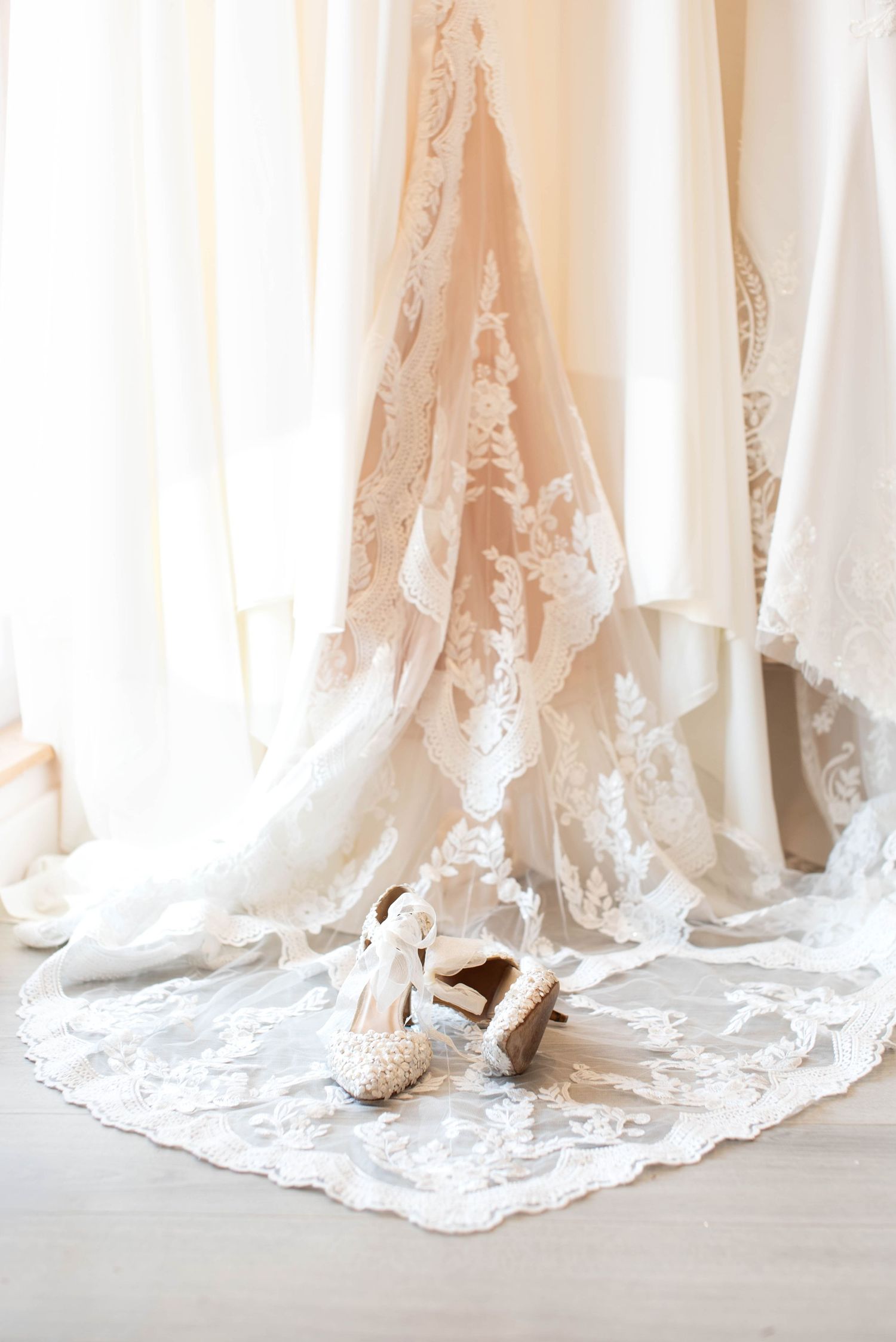 Pearl-embellished bridal heels displayed beneath a hanging lace wedding gown.
