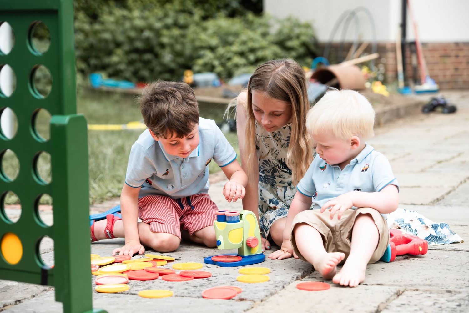 Young woman sitting outdoors playing stacking toy game with two small boys on patio.