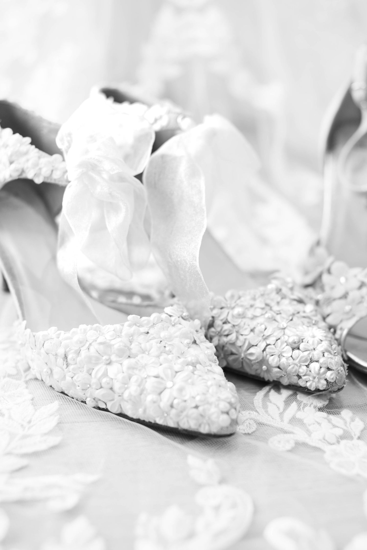 Black and white close-up of floral beaded bridal flats with white ribbon ties.