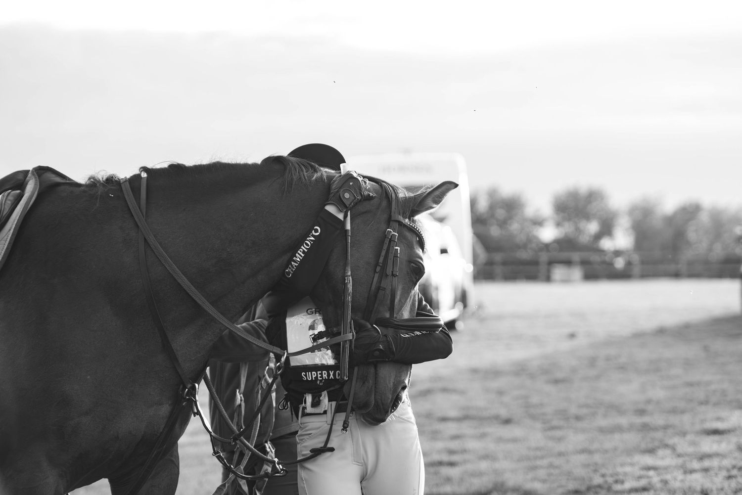 Black and white close-up of a horse wearing competition tack with a rider leaning forward at an event.